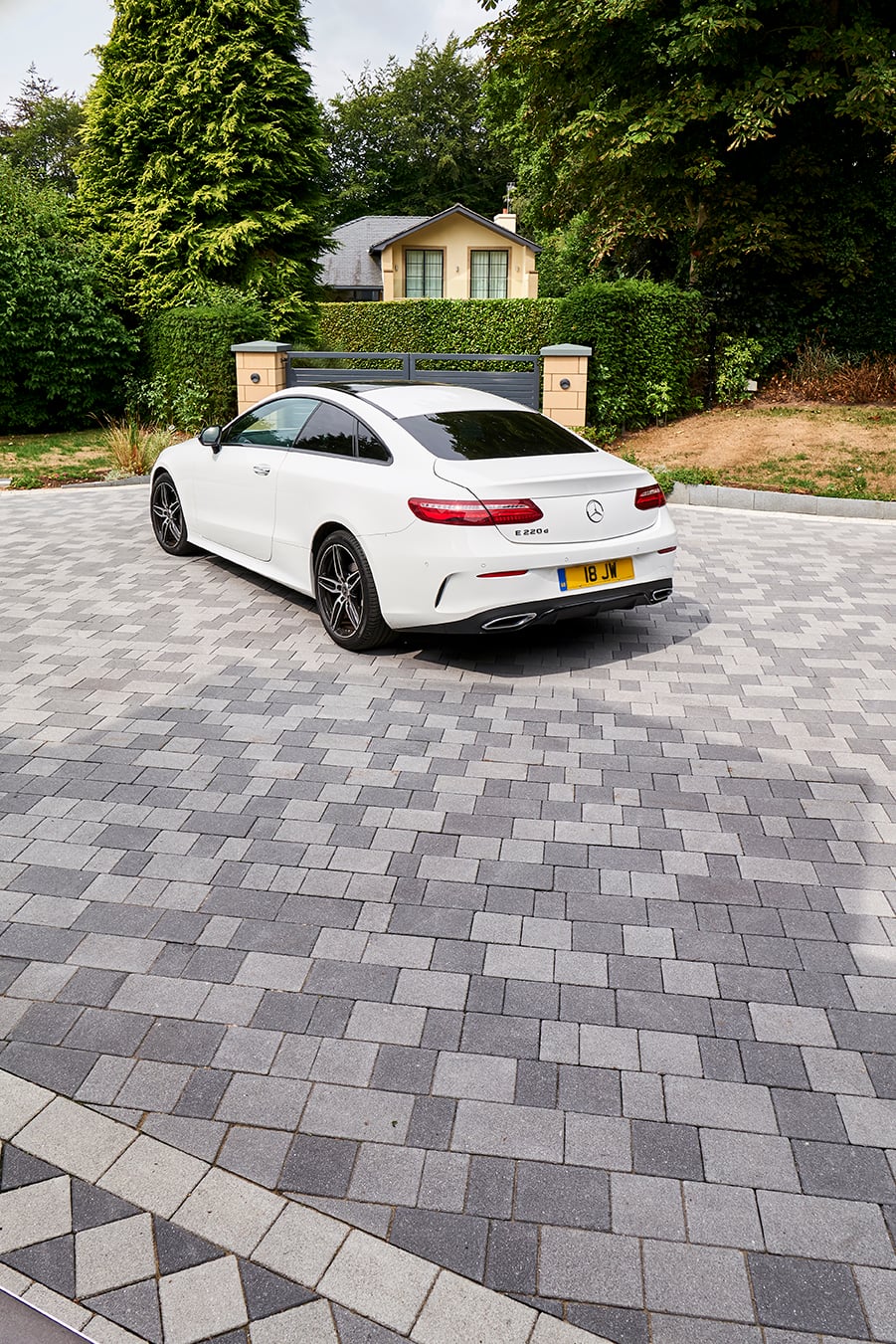 White Mercedes-Benz coupe parked on a gray block paved driveway outside a house with hedges and trees