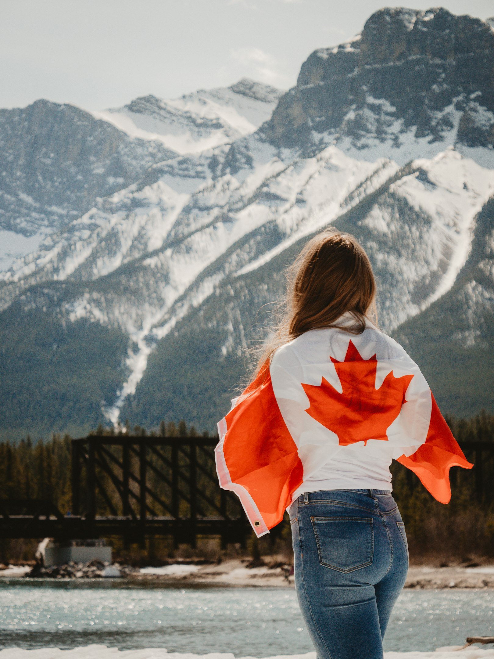Woman with Canadian flag overlooking snowy mountains and river.