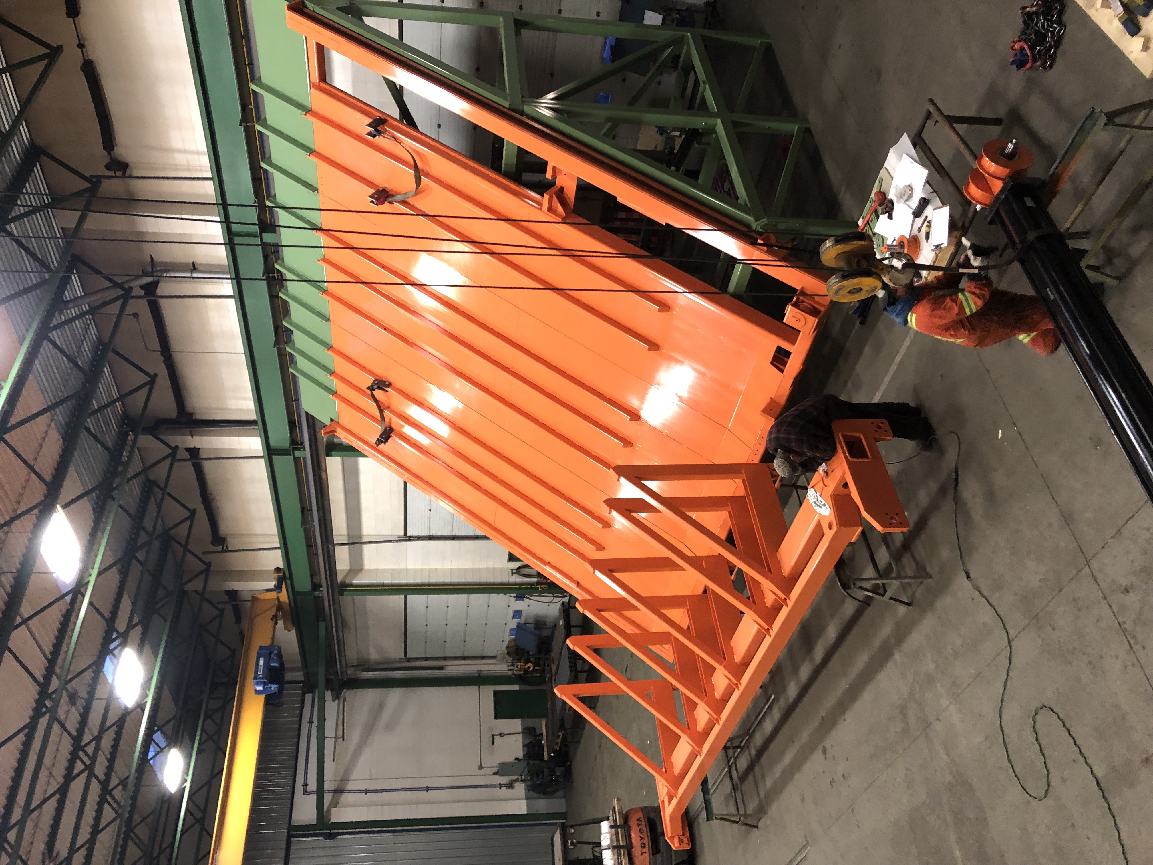 Industrial space showing large orange metal structure under construction with workers.
