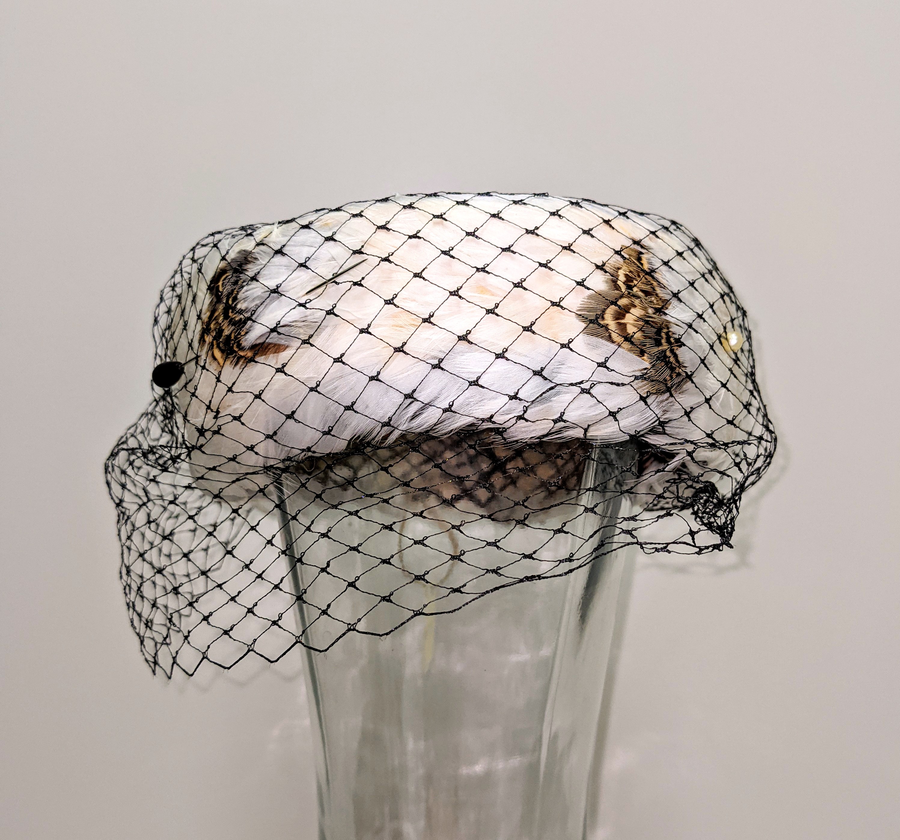 
This beautiful hat comes from the Jean Campbell collection and harkens back to fashion in the 40's. Hats were not rationed through WWII but rather were considered a luxury item and heavily taxed - sometimes up to 33%! Small hats like this one were worn askew and used hat pins to hold them in place. Though this hat has no tags or stamp to label the maker - it likely isn't homemade considering it is made of real feathers (not chicken) with a plastic veil to cover the face.

29/11/2021
2002.81 / Campbell, Jean