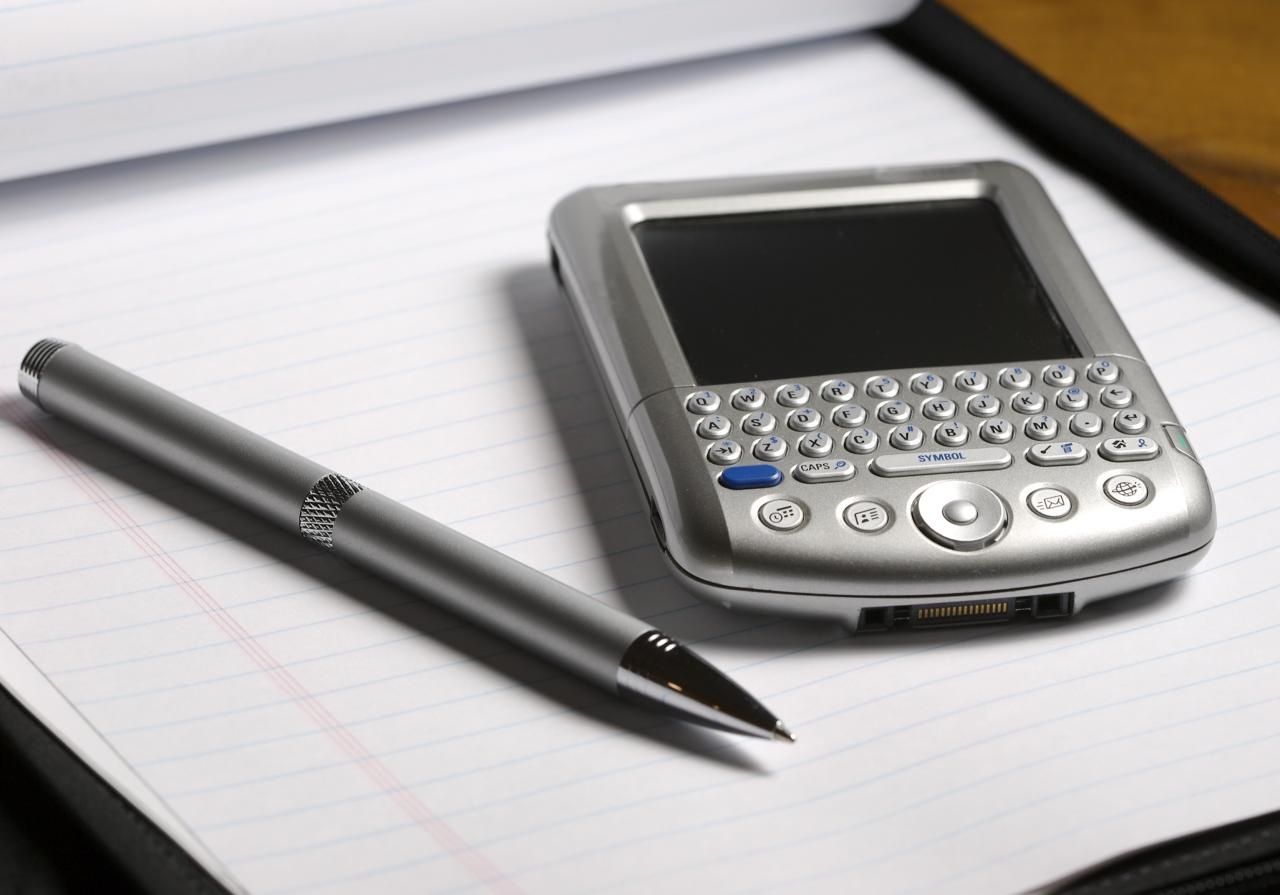 Silver PDA smartphone with QWERTY keyboard and metal pen on lined notebook Silver PDA smartphone with QWERTY keyboard and metal pen on lined notebook