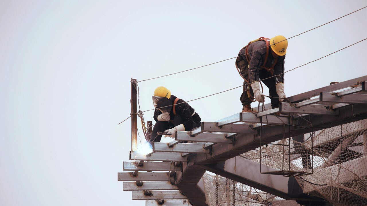 homme en veste noire et casque jaune debout sur le sommet d'un bâtiment pendant la journée homme en veste noire et casque jaune debout sur le sommet d'un bâtiment pendant la journée