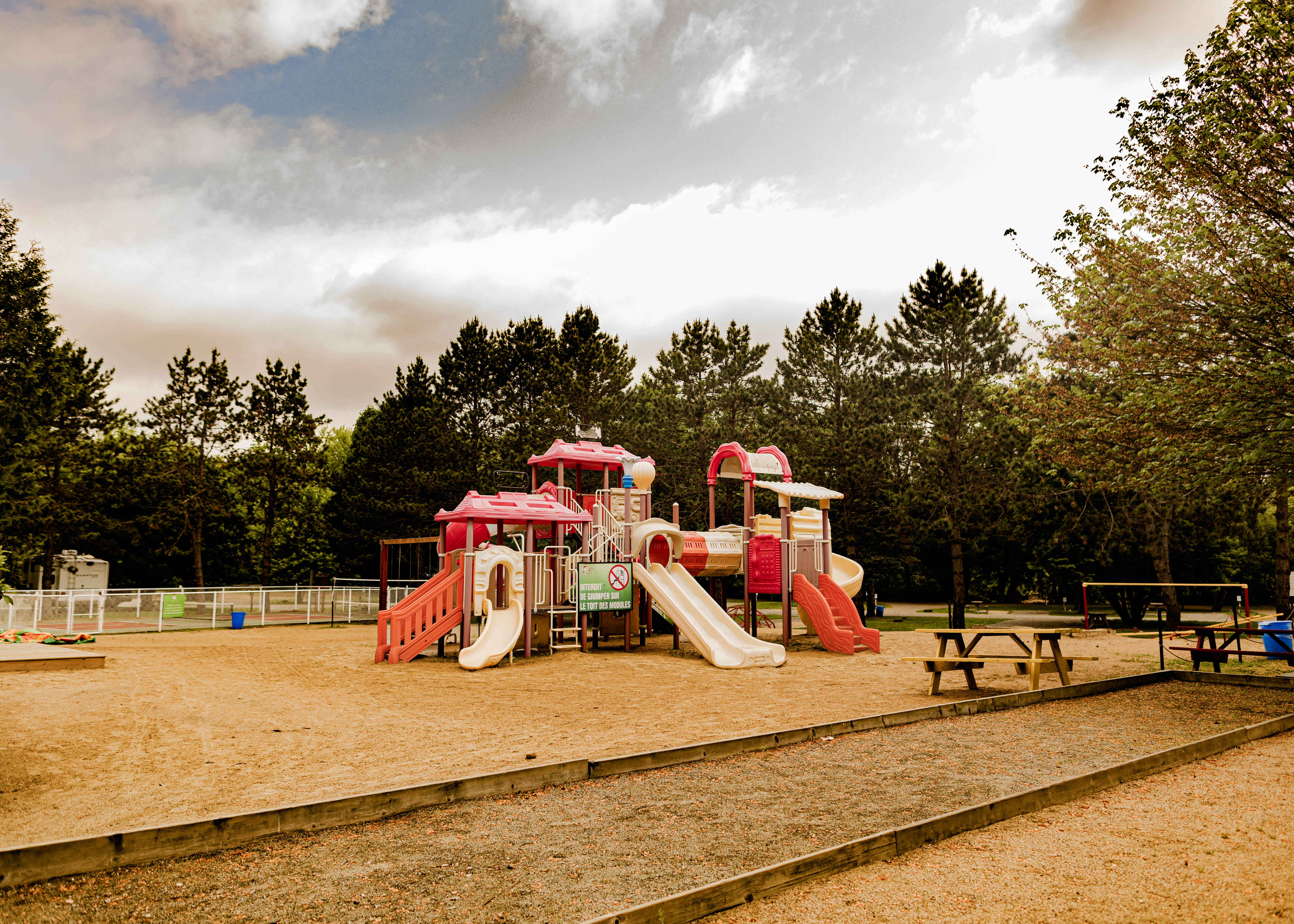 Paysage de camping en montagne avec tentes, caravanes et kayaks sur une rivière claire entourée d'arbres et montagnes.