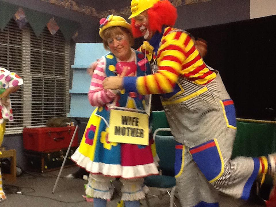 Smiling clown with colorful costume and vibrant balloons at a lively outdoor event.