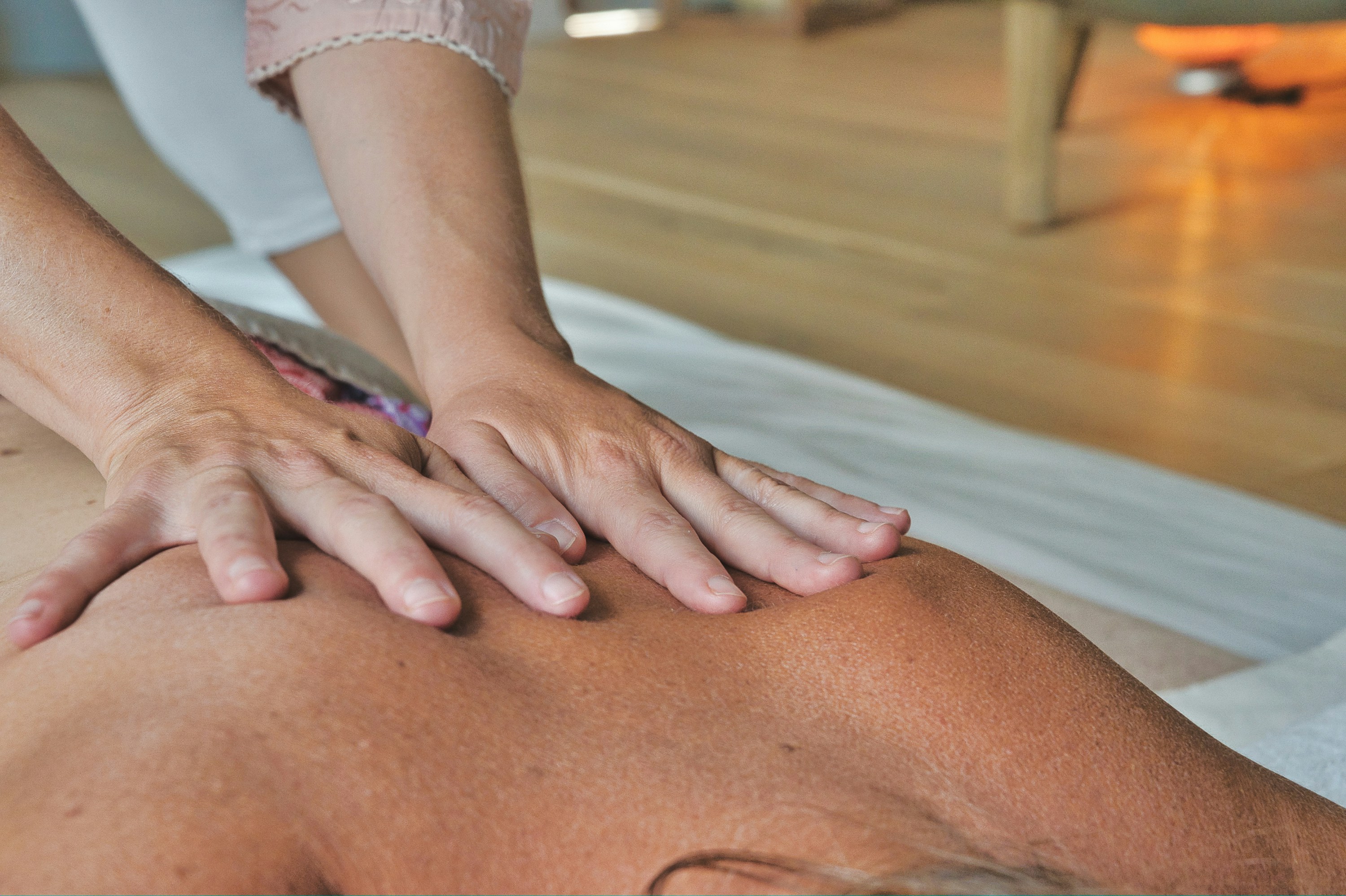 Close-up of hands giving a back massage, showcasing relaxation techniques on a serene wooden floor setting. Close-up of hands giving a back massage, showcasing relaxation techniques on a serene wooden floor setting.