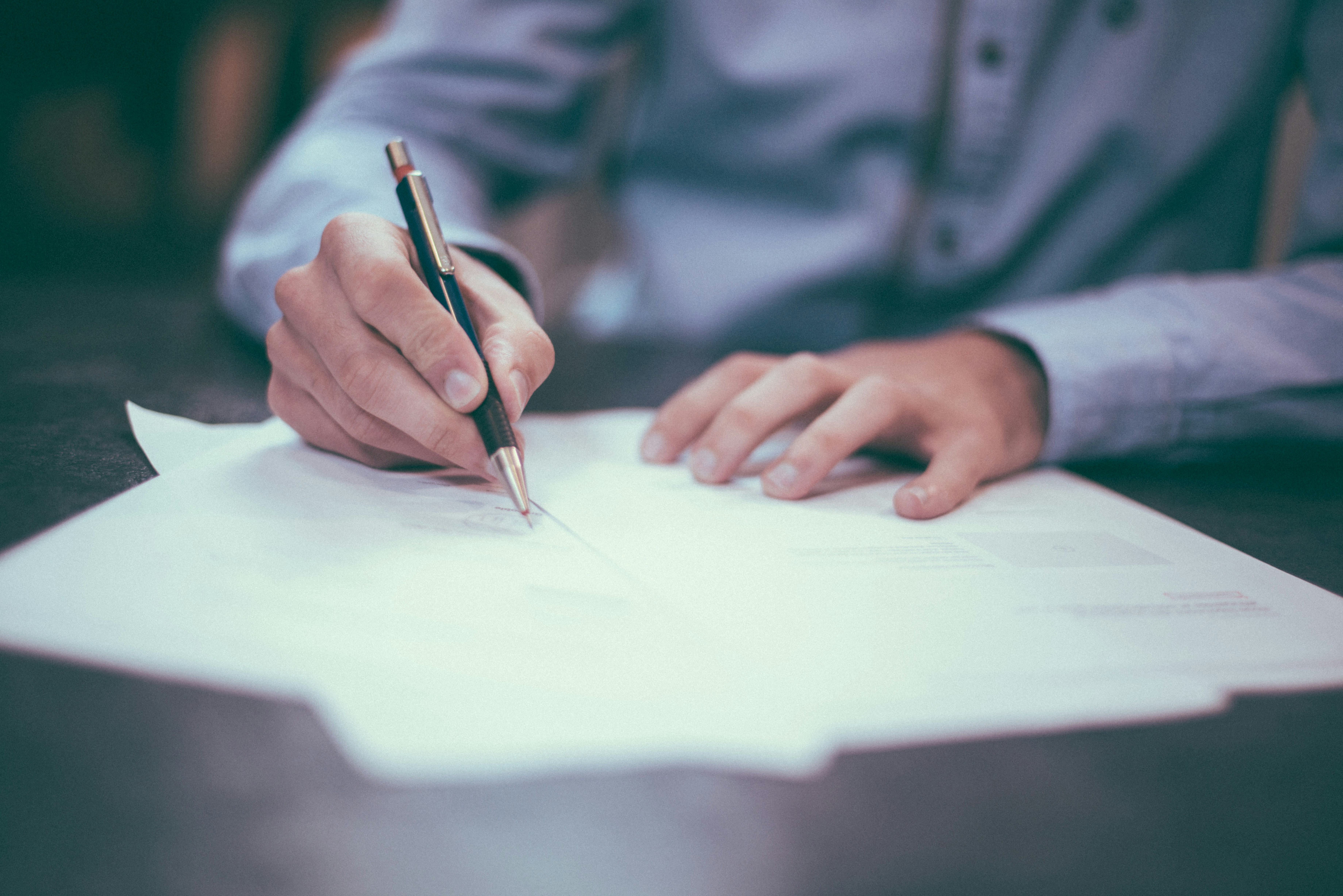 Close-up of a person in a blue shirt writing on paper with a pen.