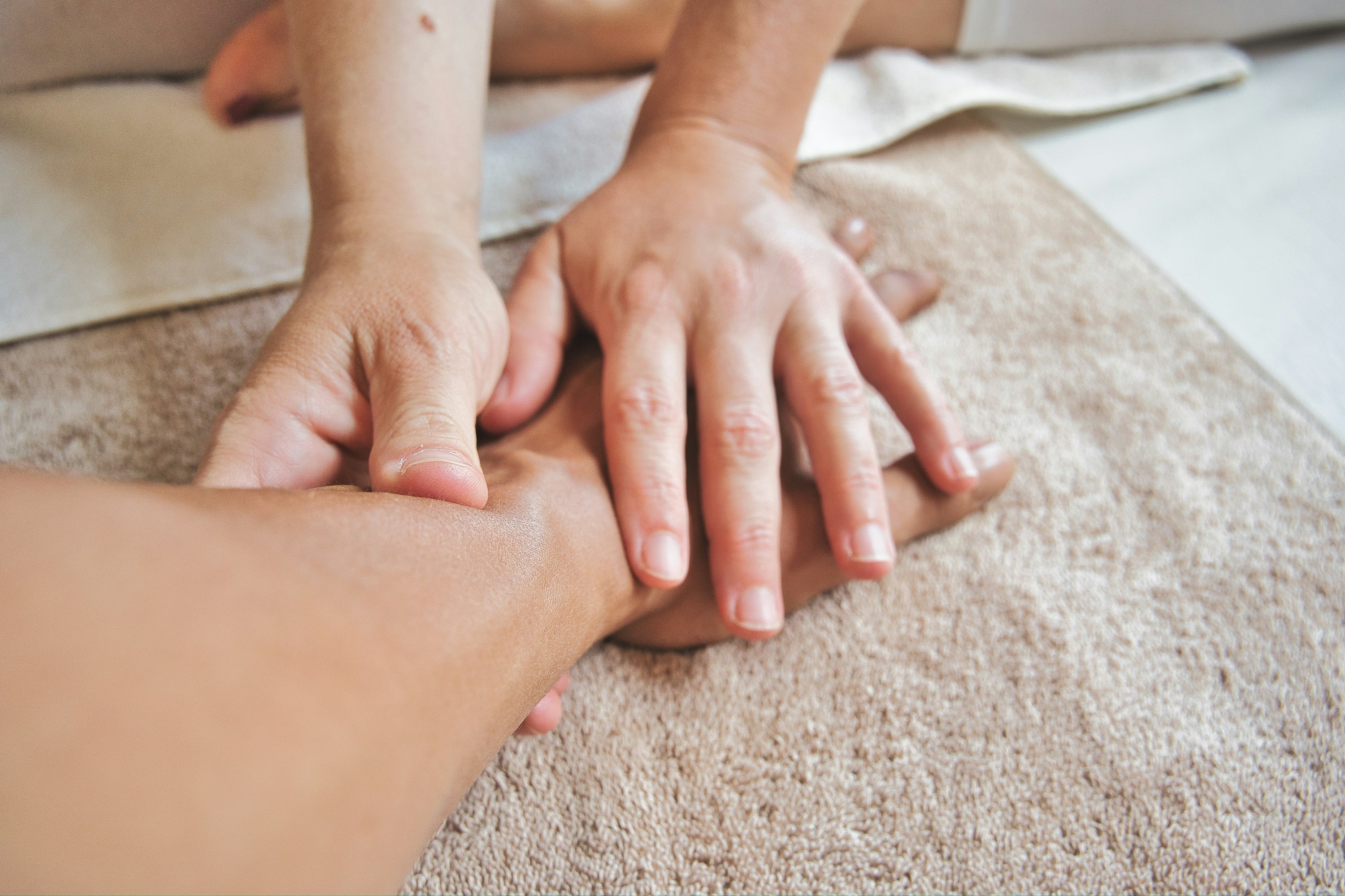 Close-up of hands performing a foot massage on a beige towel. Close-up of hands performing a foot massage on a beige towel.