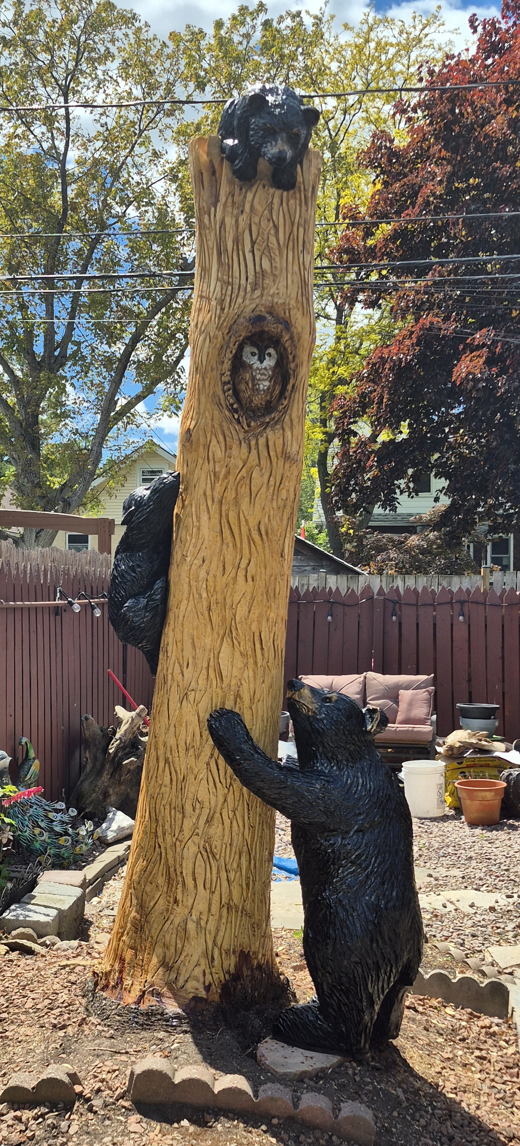 Two chainsaw wood carvers creating wooden animal sculptures in a garden with safety gear and tools
