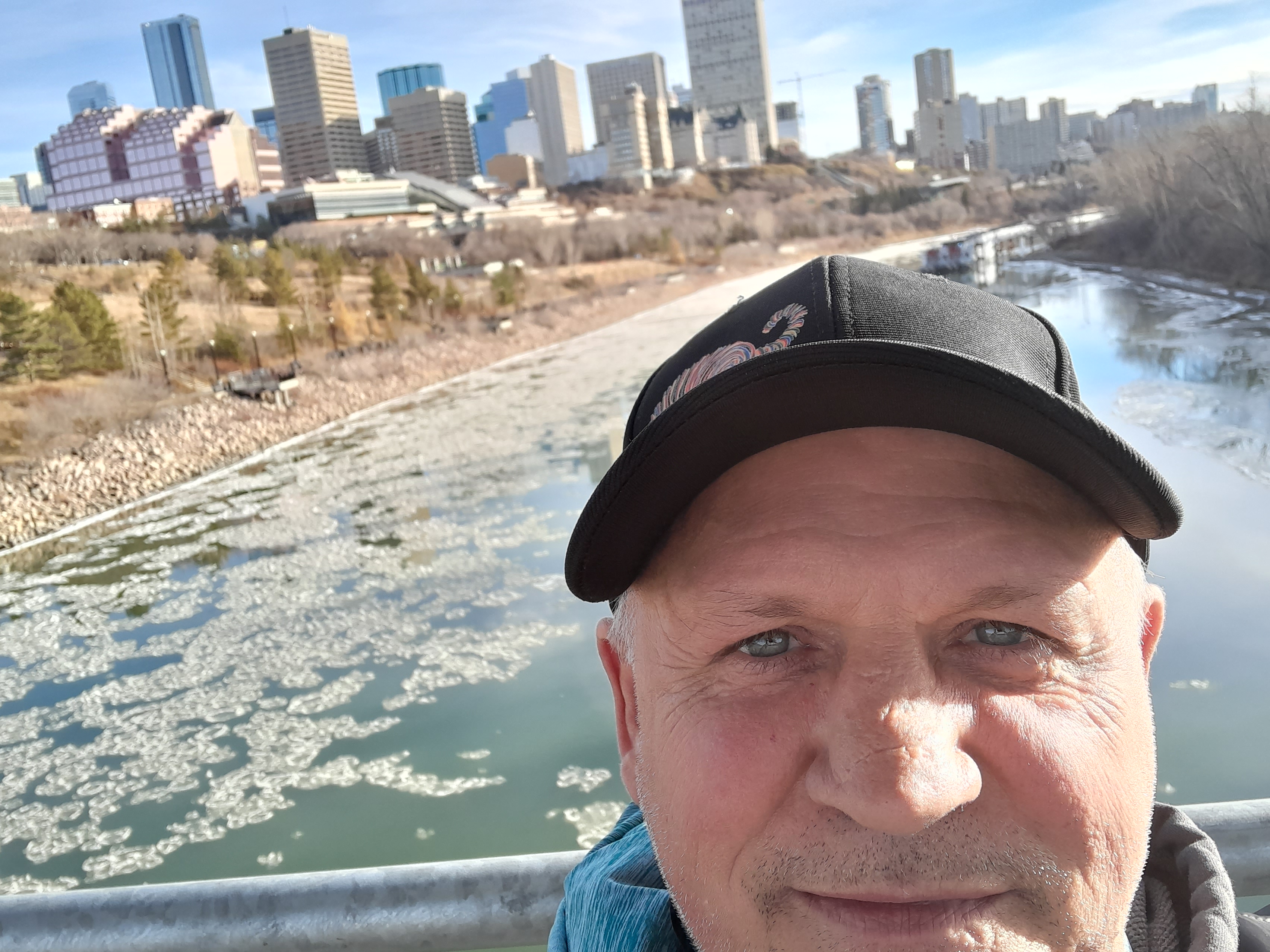 A woman wearing a mask and apron examines detergent packaging on a table in a warehouse setting, with shelves and greenery in the background.