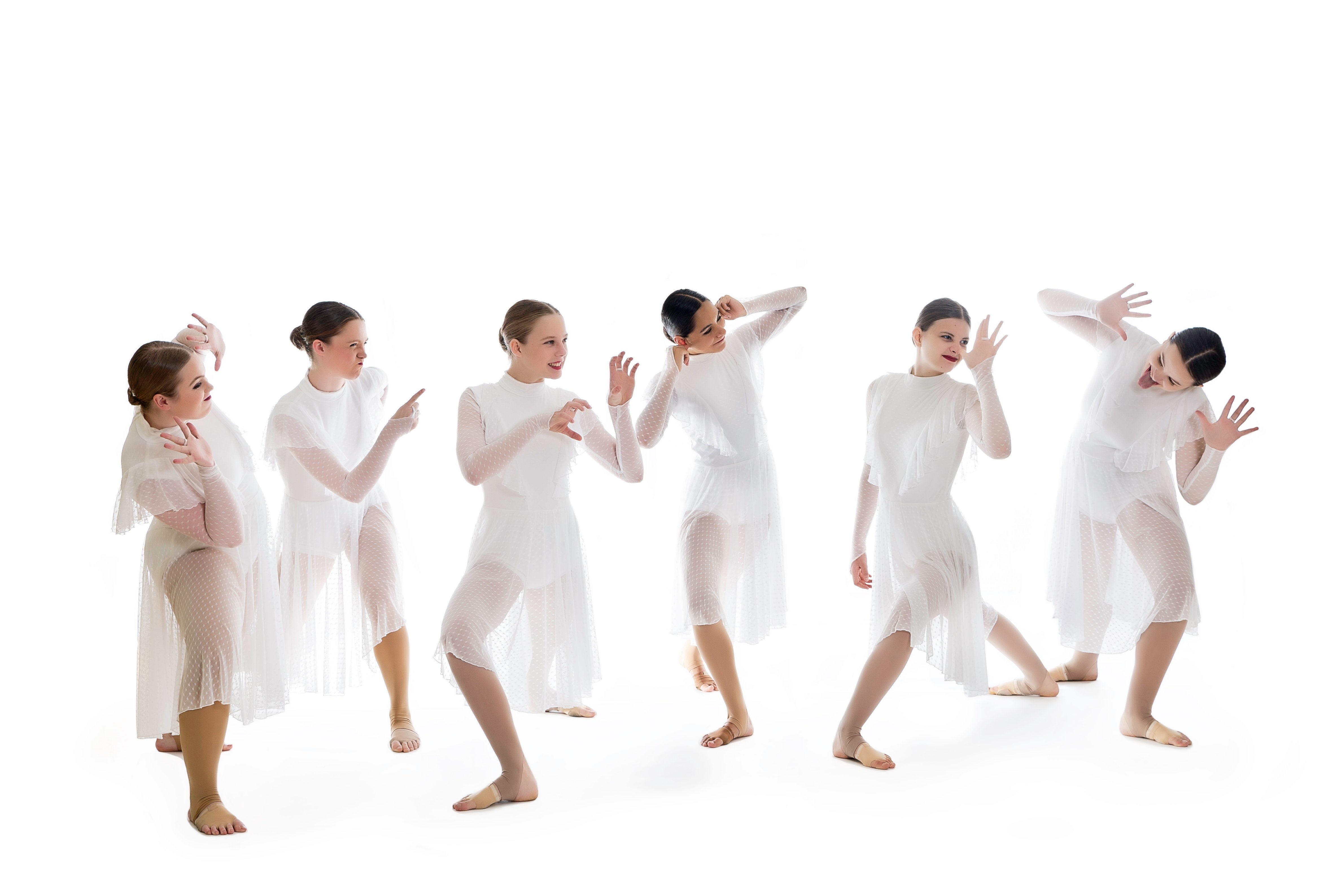 Six dancers in white dresses performing expressive movements against a white background.