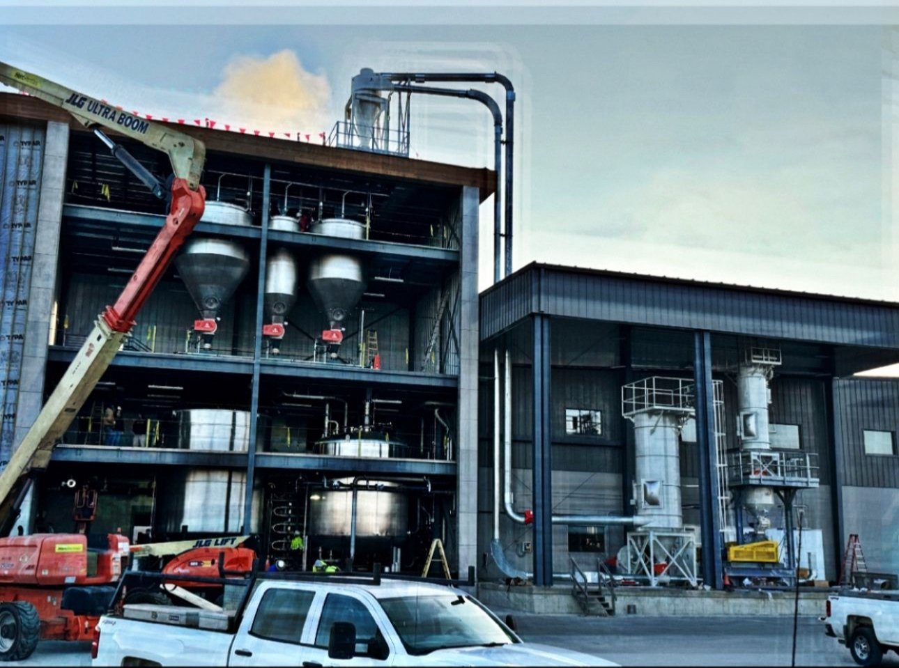 Industrial facility under construction with machinery, storage tanks, and a crane on site.