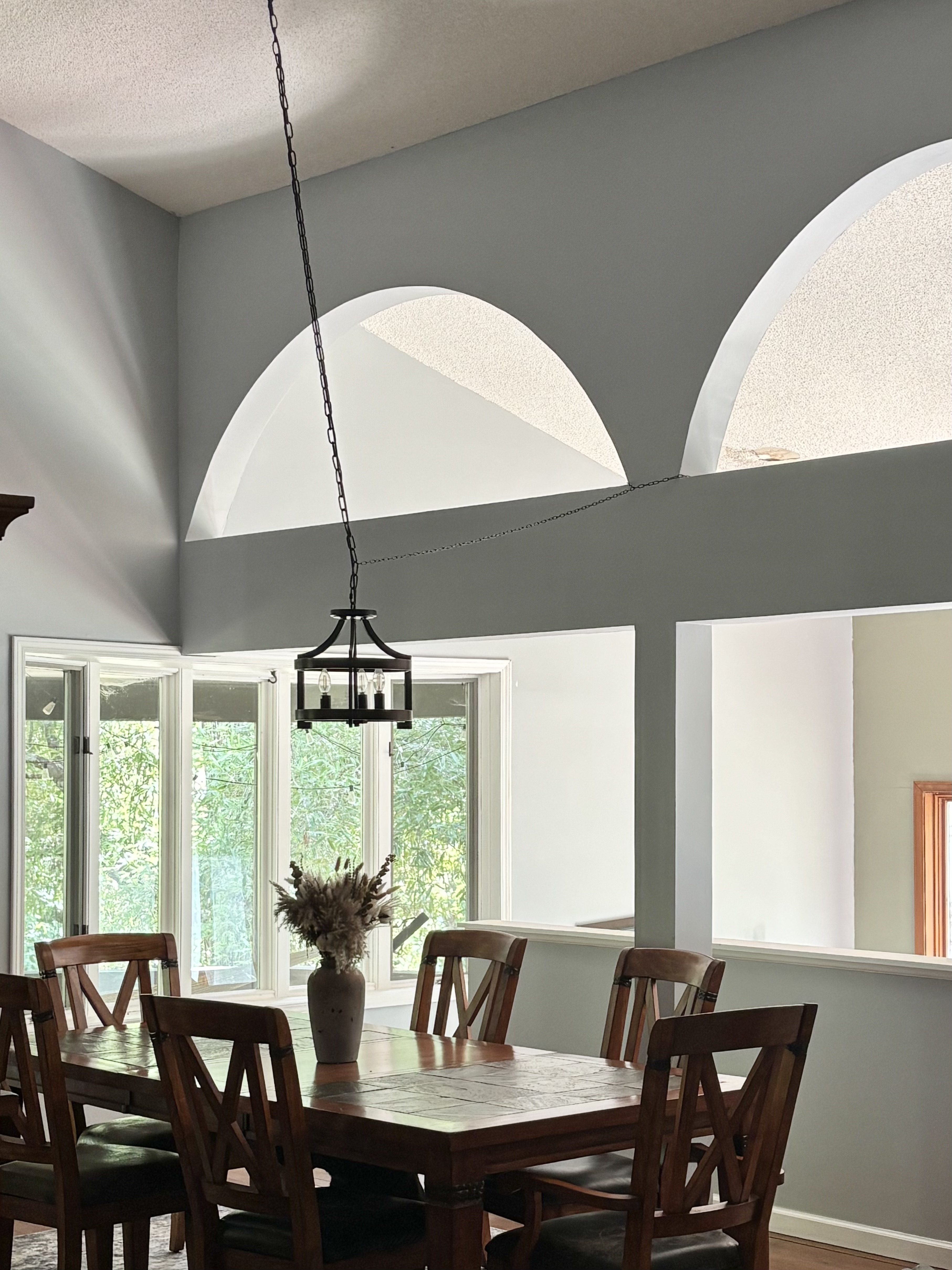 Dining room with wooden table, chairs, hanging chandelier, arched openings, and large windows