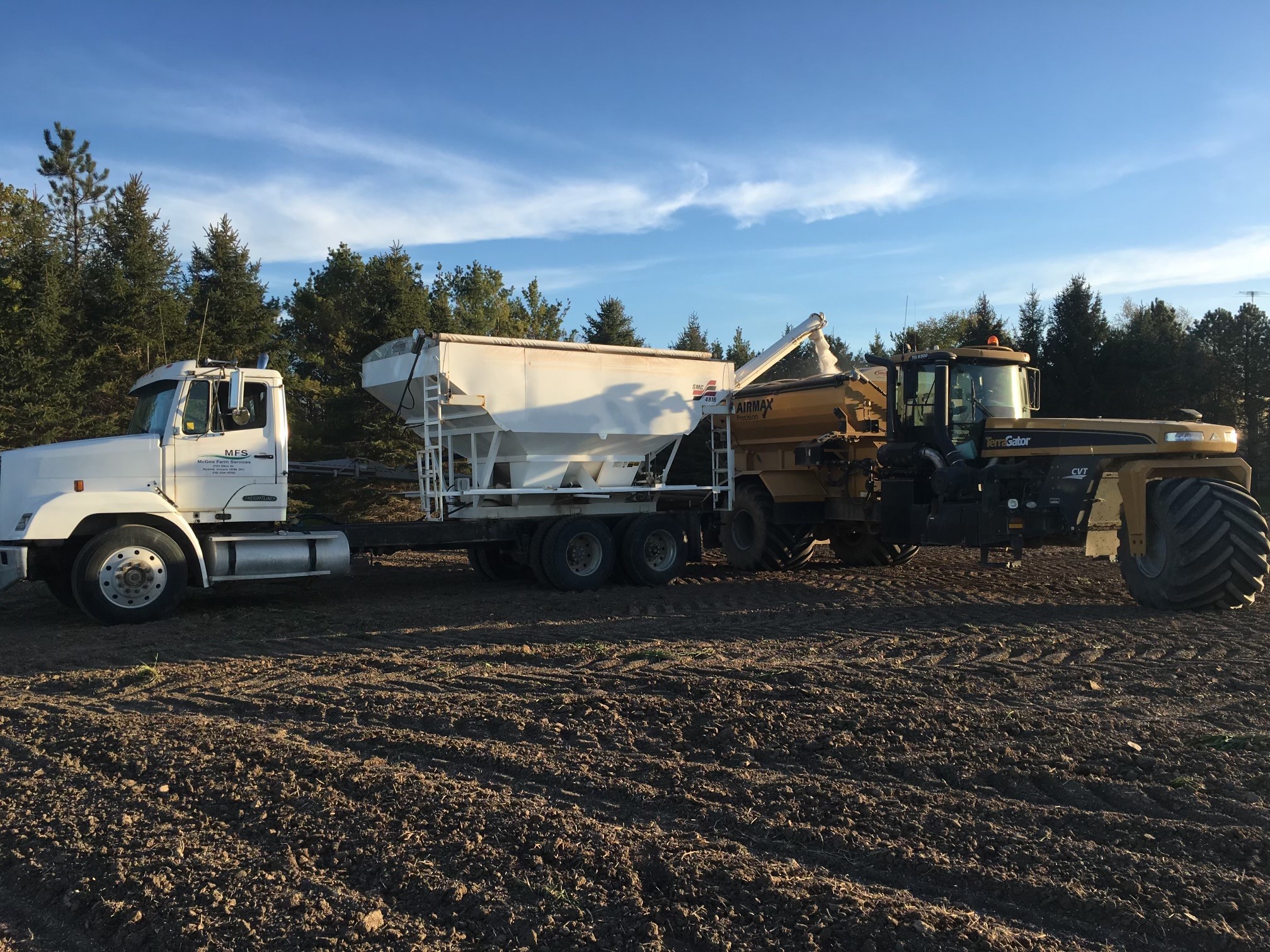 Modern farm building with green roof and signage, surrounded by lush landscape and parked cars on a sunny day.