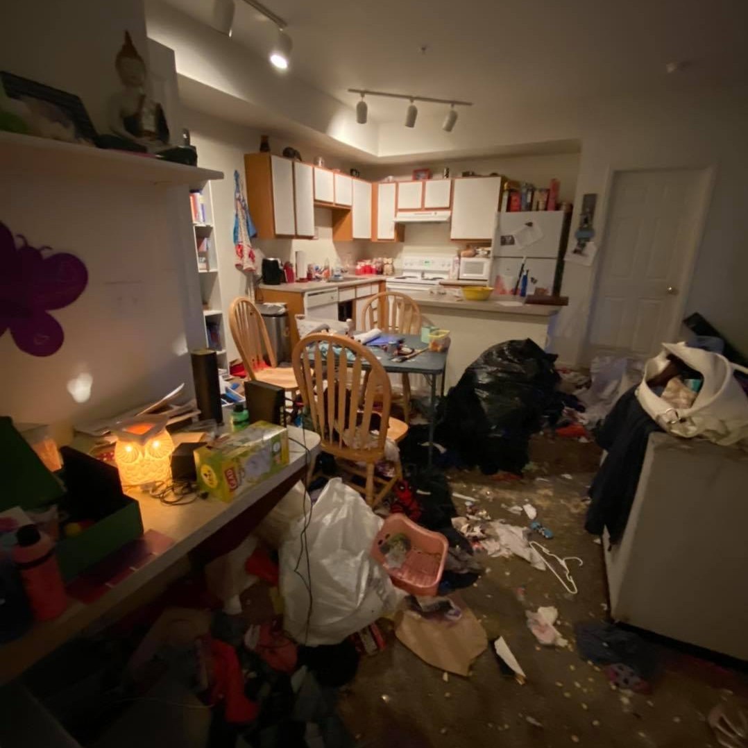 Living and kitchen area in neglected property condition with clutter accumulation, disrupted organization, and environmental overwhelm requiring structured restoration
