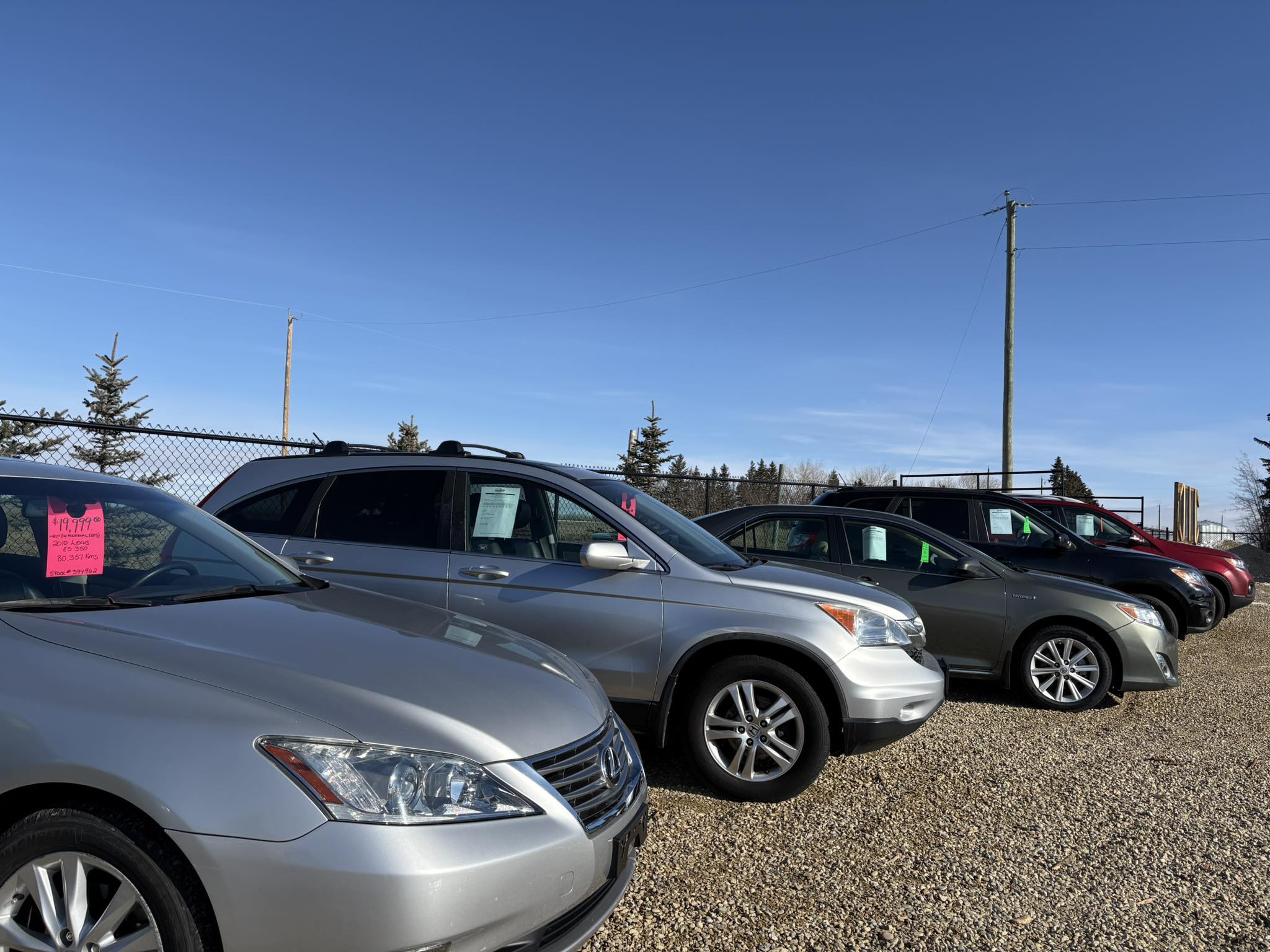 Close-up view of a car wheel on an icy and gravel-covered road, featuring alloy rims and winter tire tread design.