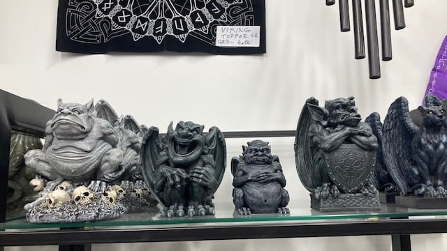 A collection of gray gargoyle statues with various expressions on a glass shelf, surrounded by decorative items.