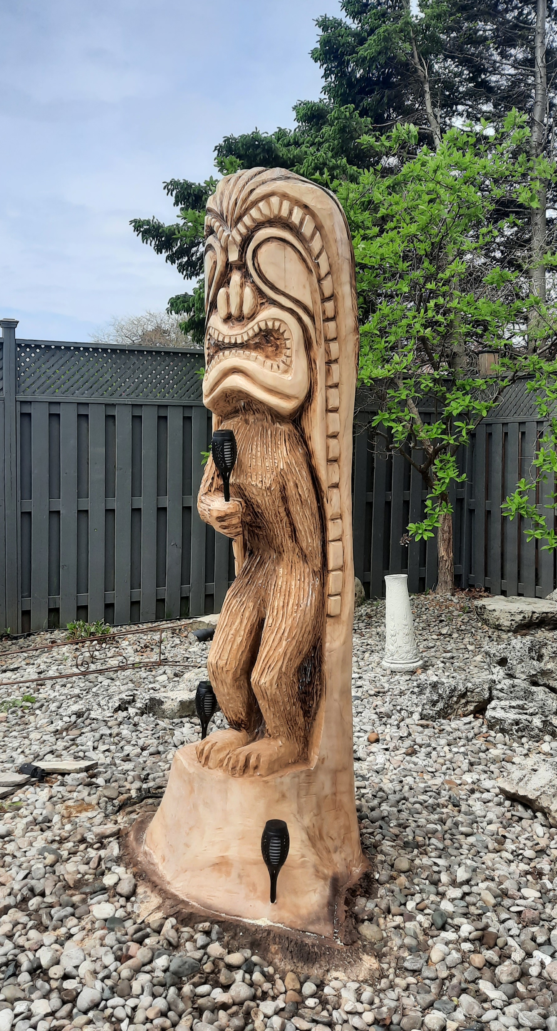 Two wood carvers using chainsaws to create wooden animal sculptures in a backyard garden