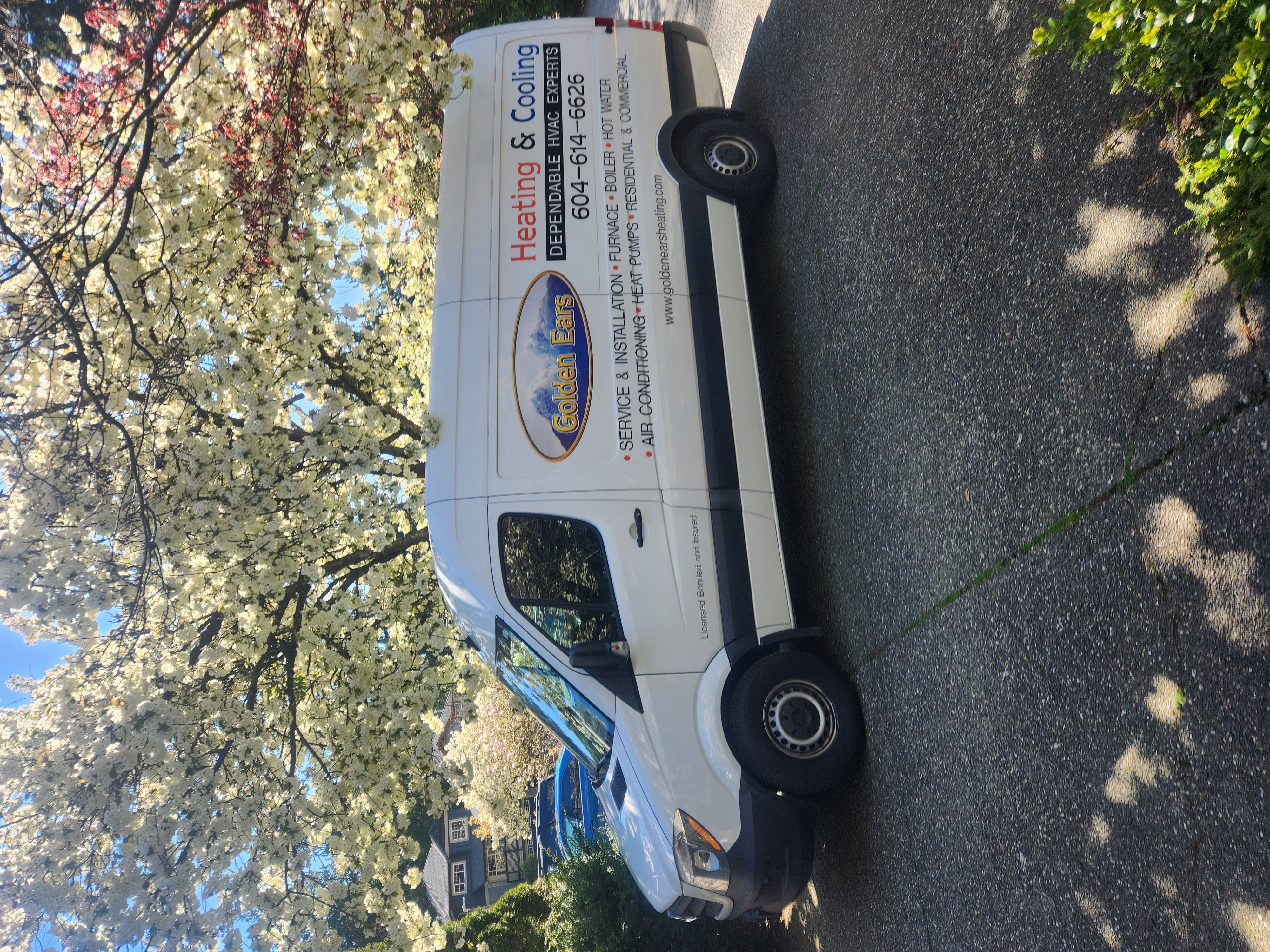 Delivery truck parked in front of a modern building with a logo, surrounded by greenery and clear skies.