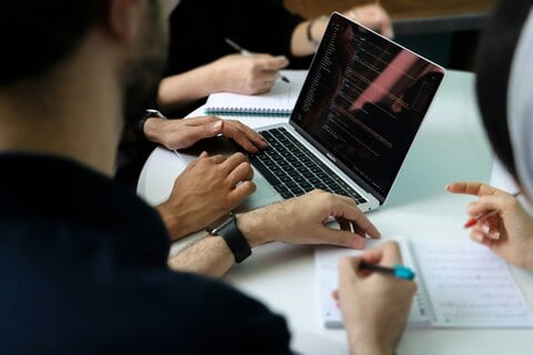 Team collaborating around laptop displaying code during a business meeting Team collaborating around laptop displaying code during a business meeting