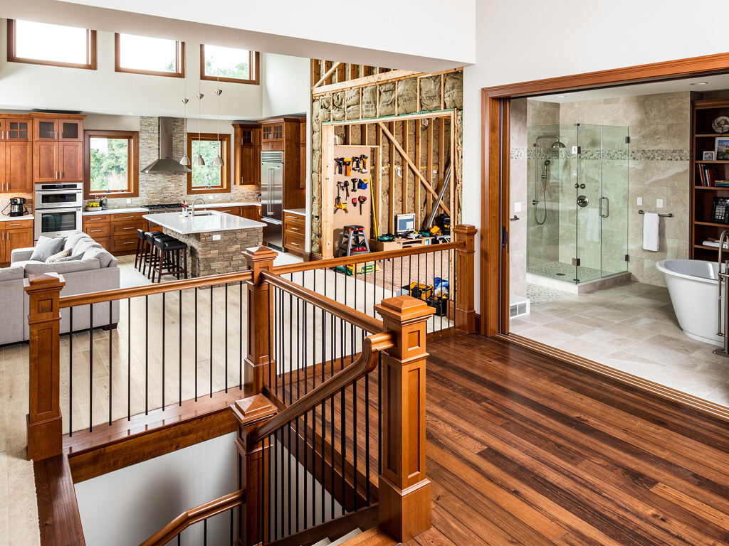 Luxury home renovation showing open kitchen, exposed framing, hardwood staircase, and modern bathroom with glass shower