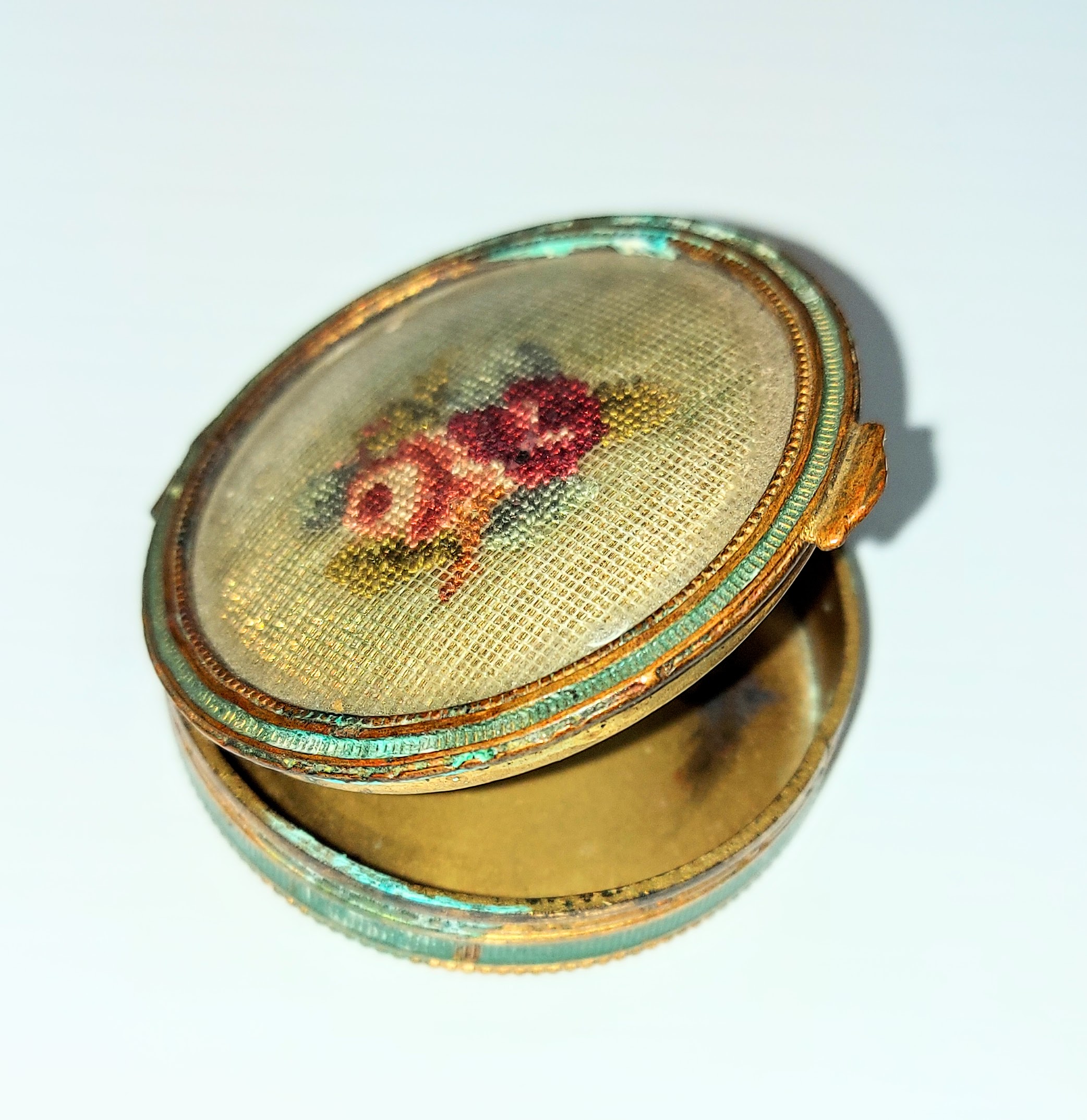 This small case is a makeup compact. On the interior of the lid is a small mirror and though it is mostly empty there are still trace amounts of powder in the base. The floral pattern on the top is intricate needlepoint work - safely held behind a piece of glass. The turquoise color comes from a tarnish on the brass metal of the compact. There is no brand or date labelled on the object but likely dates back to the 40's.
2003.34.02 / Bundy, Val
13/03/2023