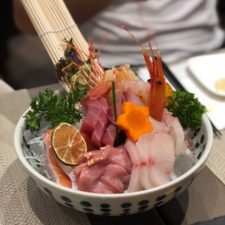 Close-up of fresh sashimi plated with garnishes, including green leaves and wasabi, served on a decorative dish.