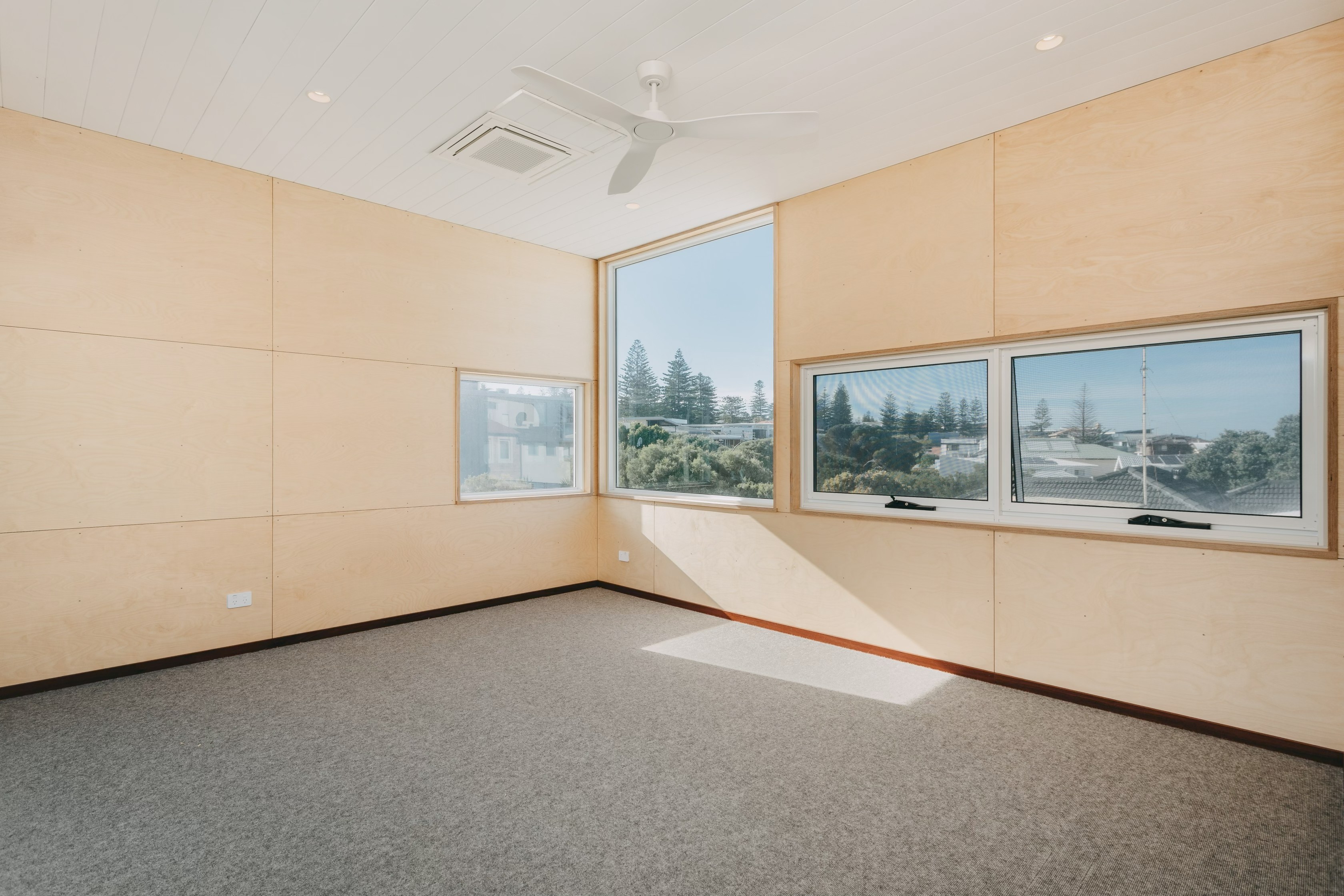 Modern kitchen interior with wooden cabinets, marble backsplash, central island, and a cozy living area with a gray sofa and potted plant.