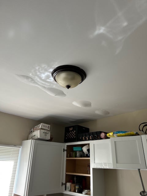Ceiling with light fixture and water damage above kitchen cabinets.