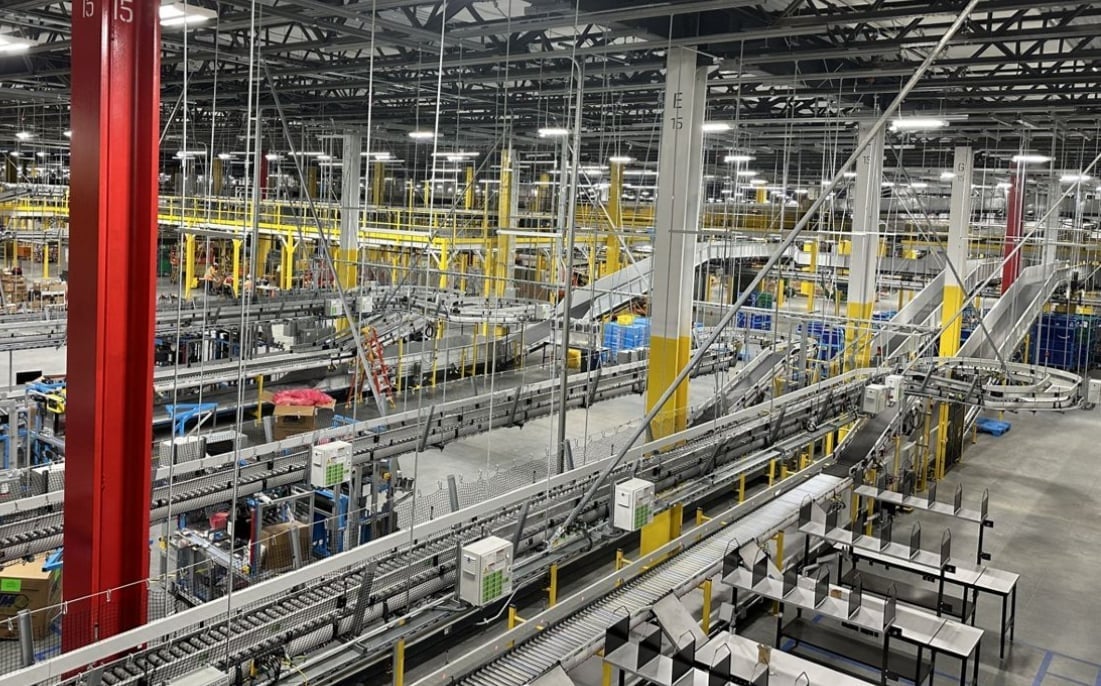 Modern warehouse interior with extensive conveyor belt system, yellow and red support beams, and rows of packaging stations.
