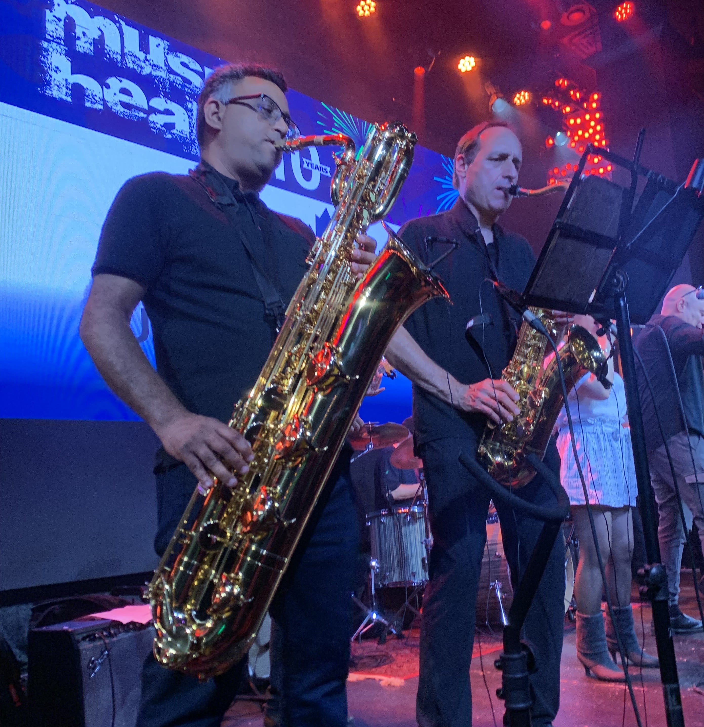 Saxophone players performing live on stage with colorful concert lights and band backdrop
