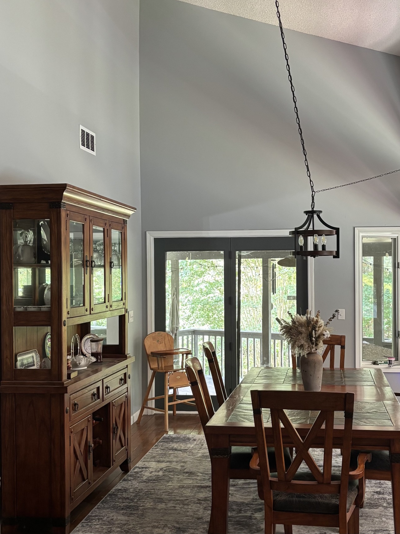 Rustic dining room with wooden table, china cabinet, sliding glass doors, and black chandelier