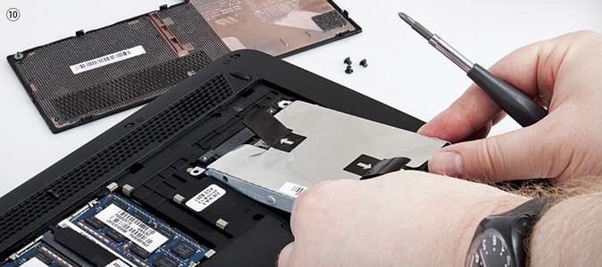 Person installing a hard drive into a laptop with a screwdriver and visible RAM modules.