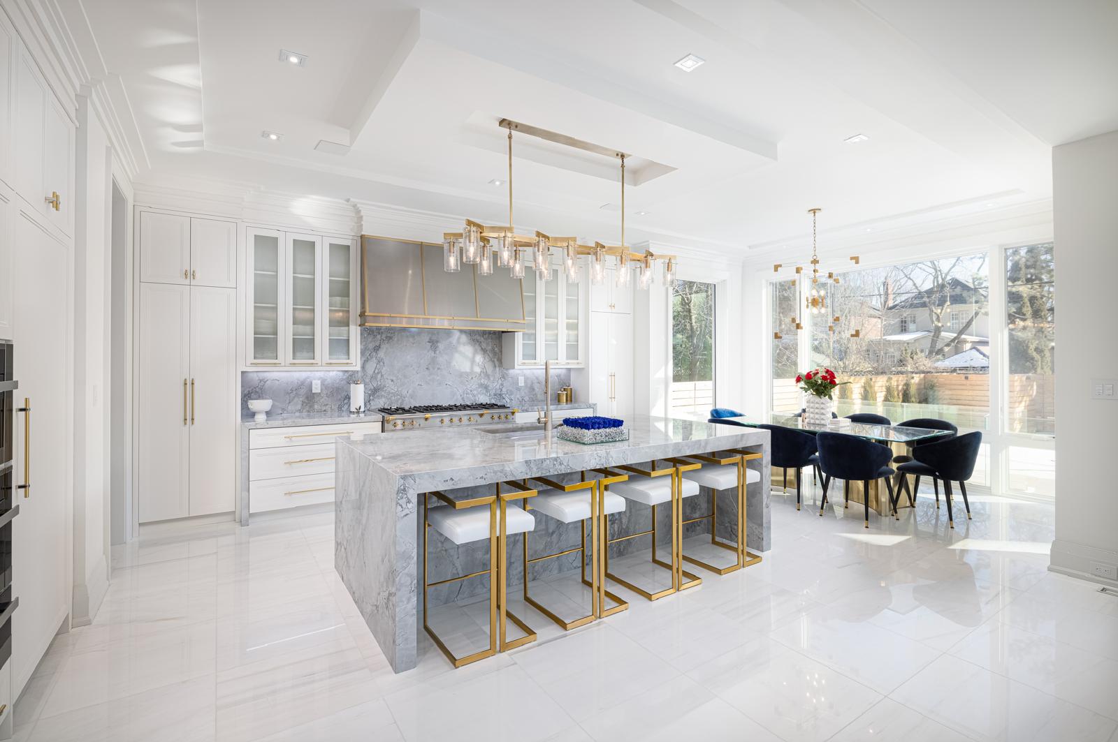 Luxurious modern kitchen with marble island, gold accents, and elegant dining area with blue velvet chairs.