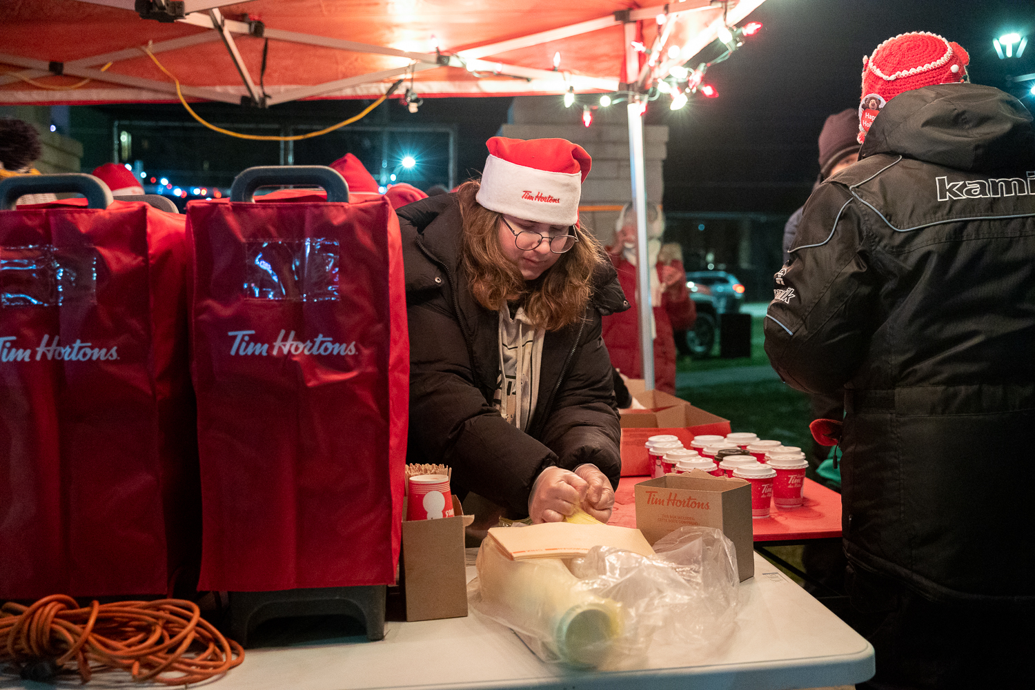 Winter evening scene with snow-covered path, illuminated string lights, people walking, and decorated pavilions.
 Winter evening scene with snow-covered path, illuminated string lights, people walking, and decorated pavilions.