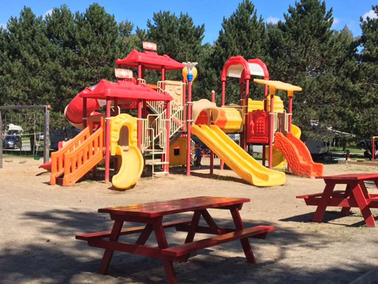 Paysage de camping en montagne avec tentes, caravanes et kayaks sur une rivière claire entourée d'arbres et montagnes.