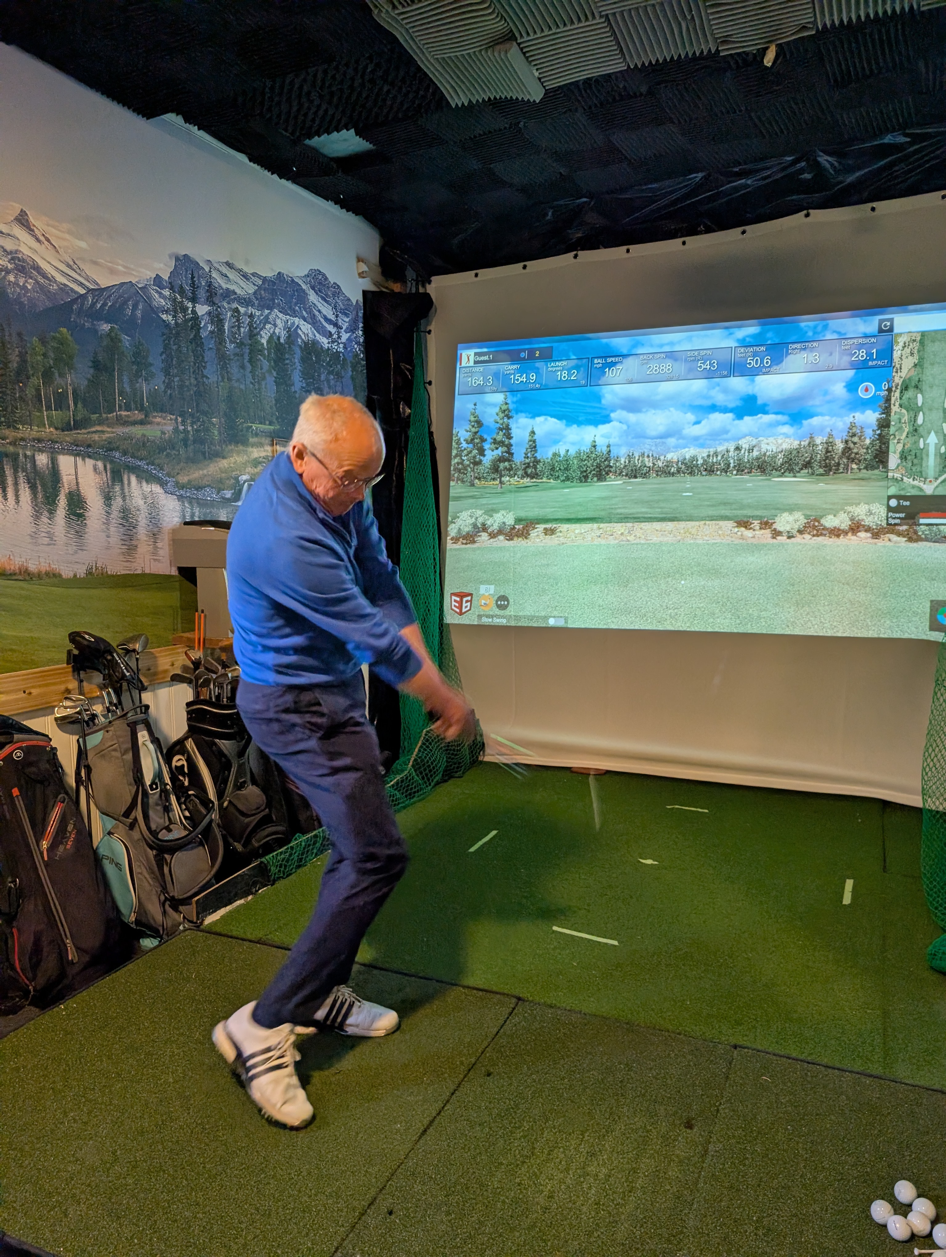 Man swinging golf club in indoor simulator with scenic mountain backdrop. Man swinging golf club in indoor simulator with scenic mountain backdrop.