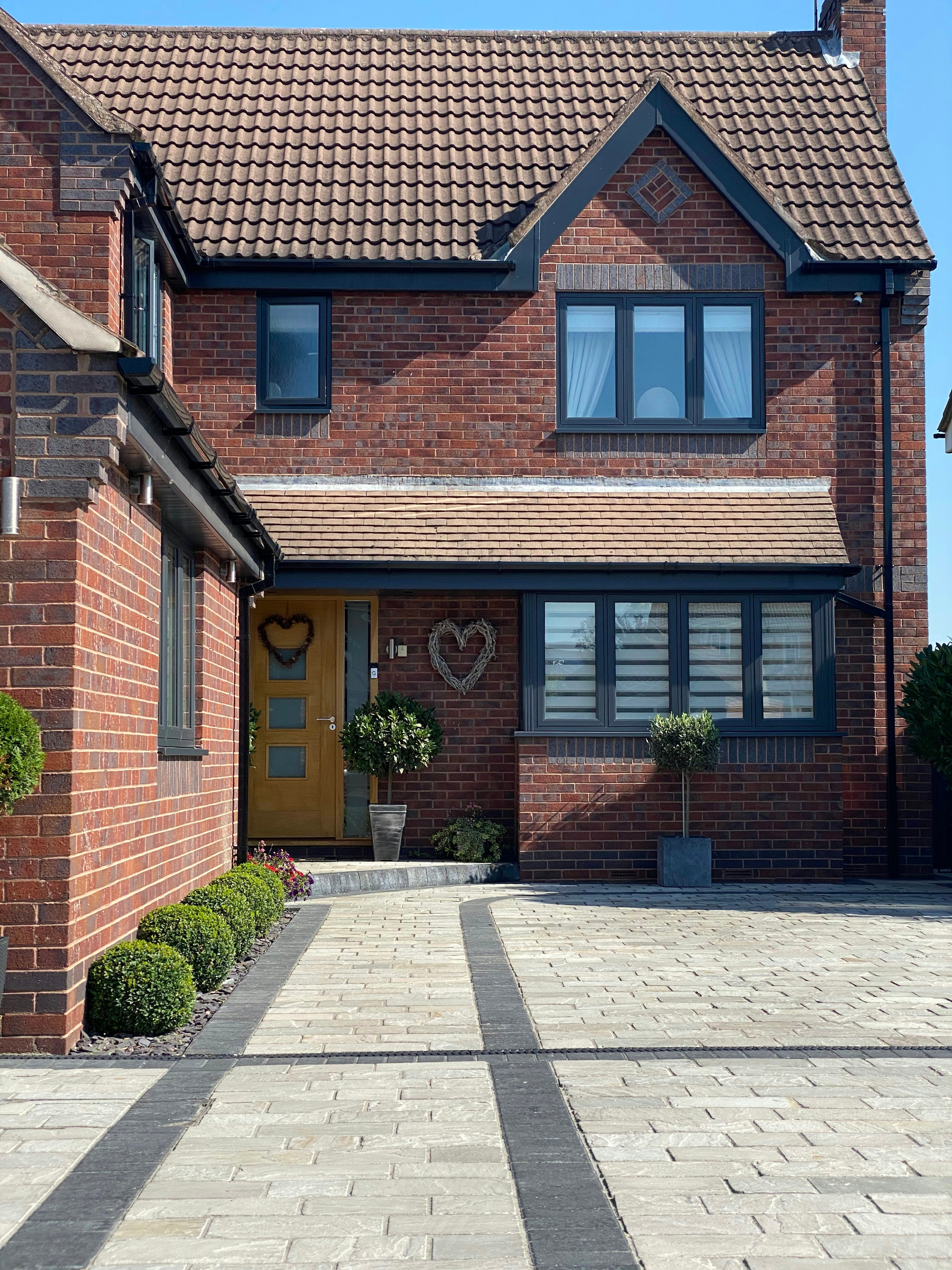 Modern red brick house with tiled roof, gray windows, paved driveway, and landscaped front entrance