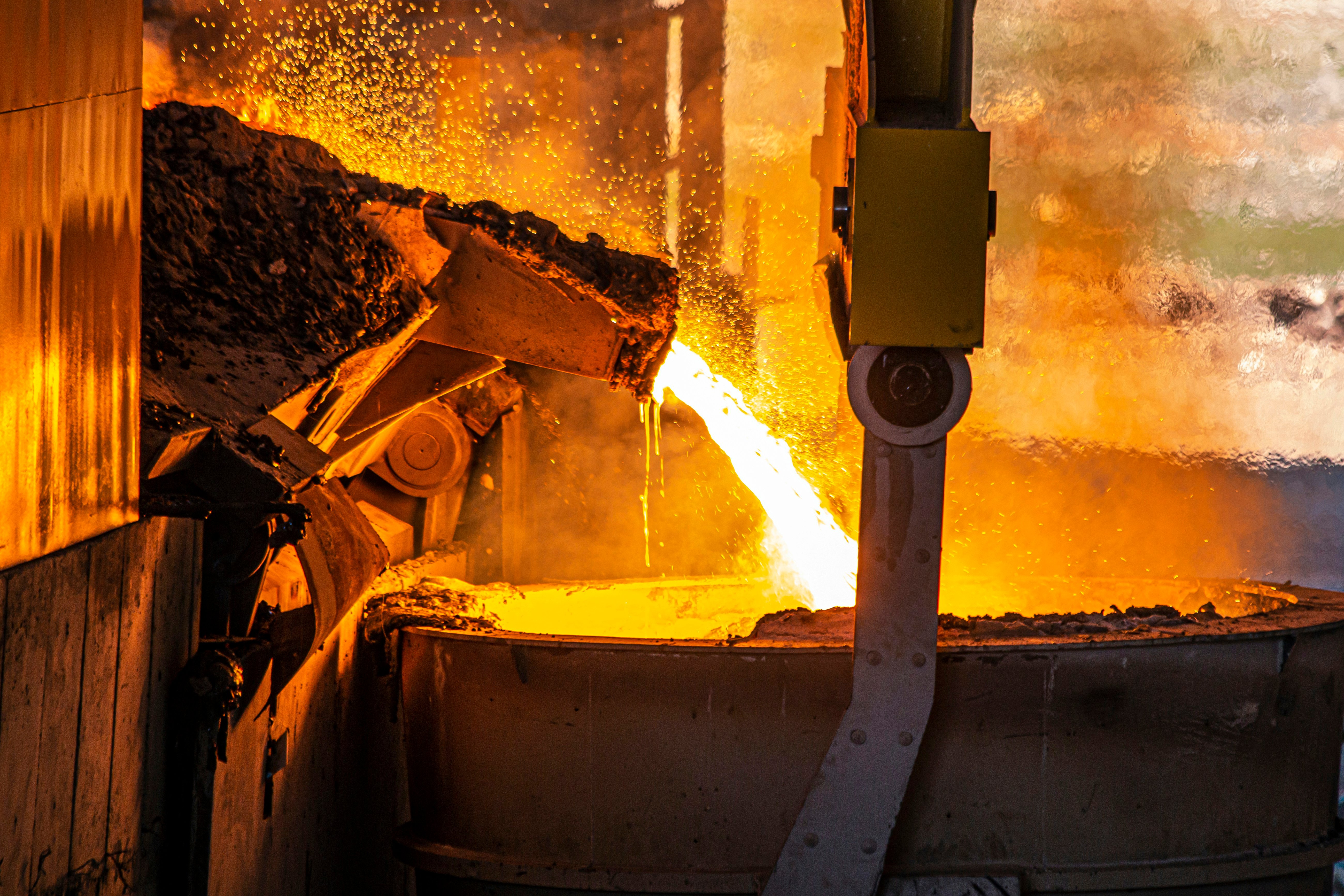 Molten metal pouring into a container in a foundry, with sparks and intense orange glow, depicting industrial metal casting process. Molten metal pouring into a container in a foundry, with sparks and intense orange glow, depicting industrial metal casting process.