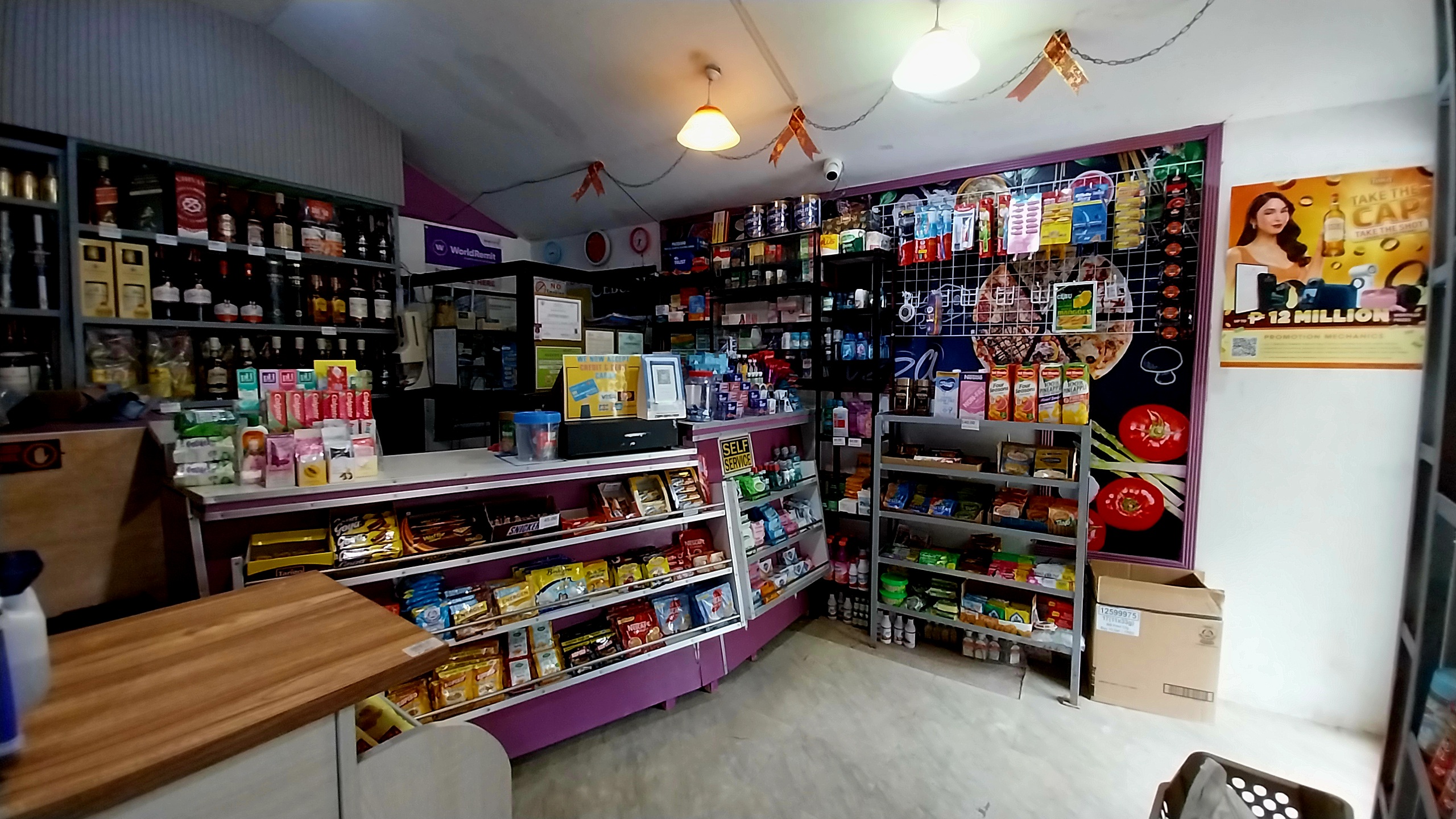 Interior of a convenience store with shelves stocked with snacks, drinks, toiletries, and various goods under bright lighting.