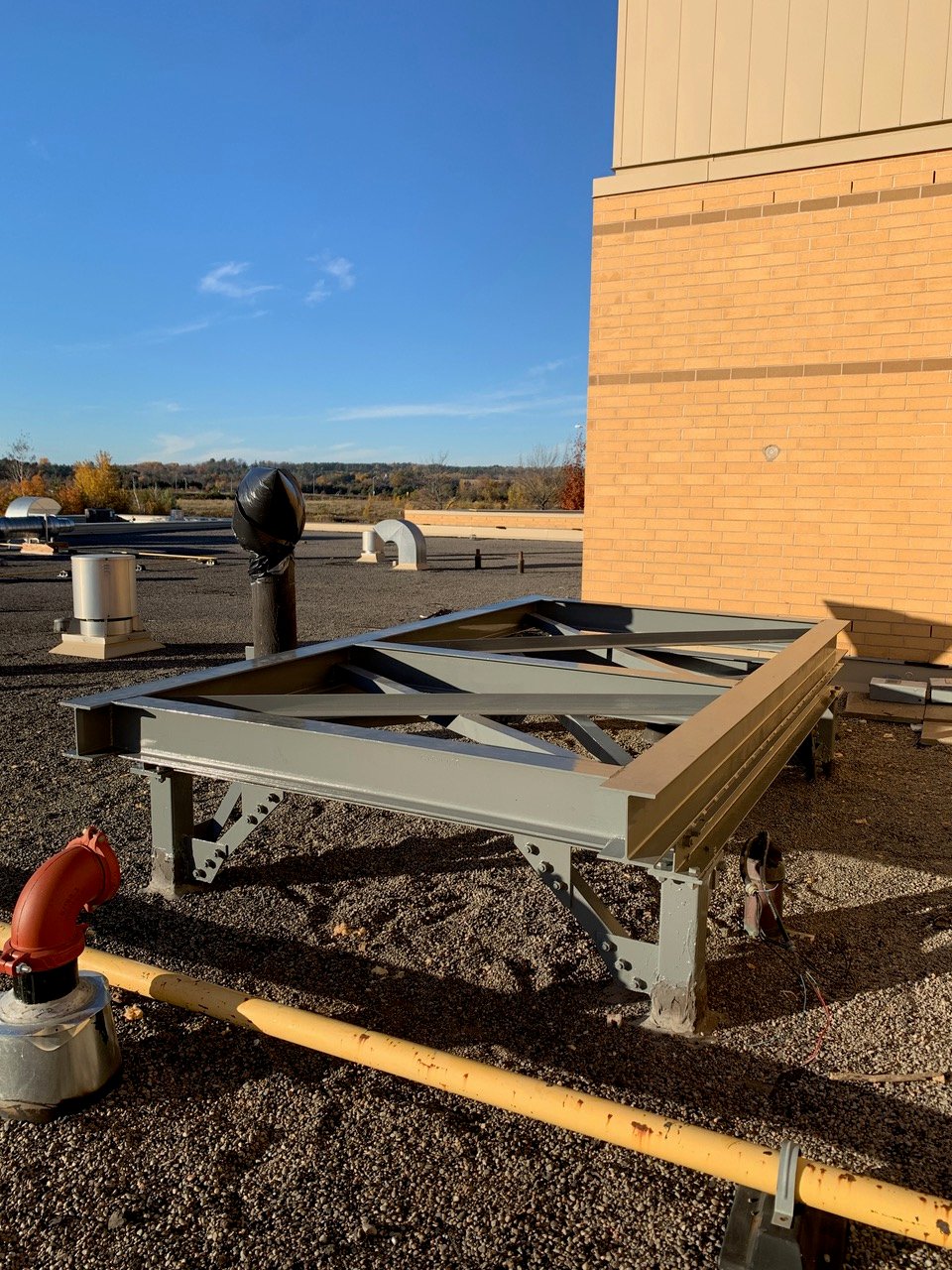 Rooftop with steel framework and ventilation pipes under a clear blue sky.