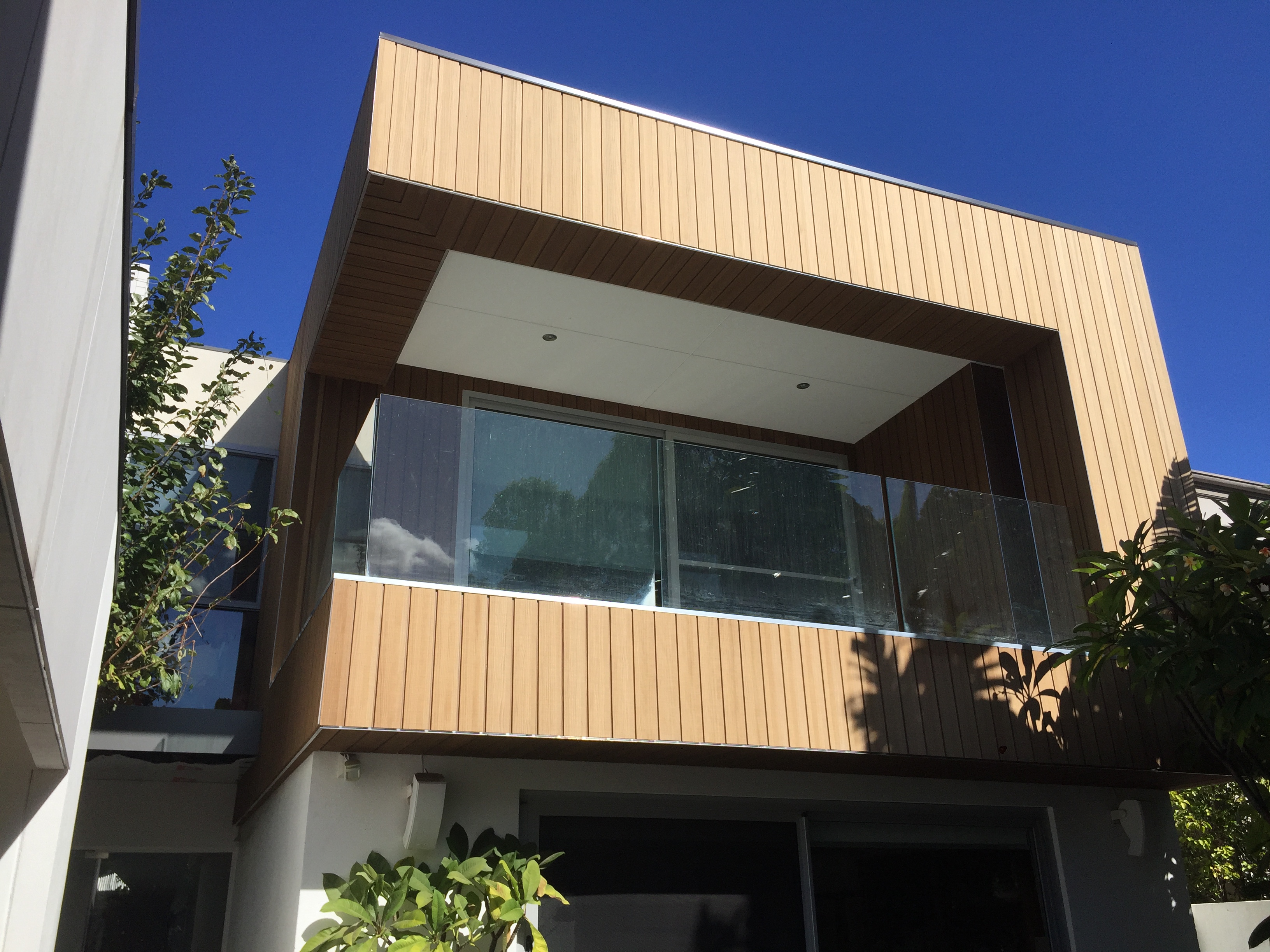 Modern kitchen interior with black cabinets, large island, pendant lighting, and sliding glass doors opening to outdoor dining area with greenery.