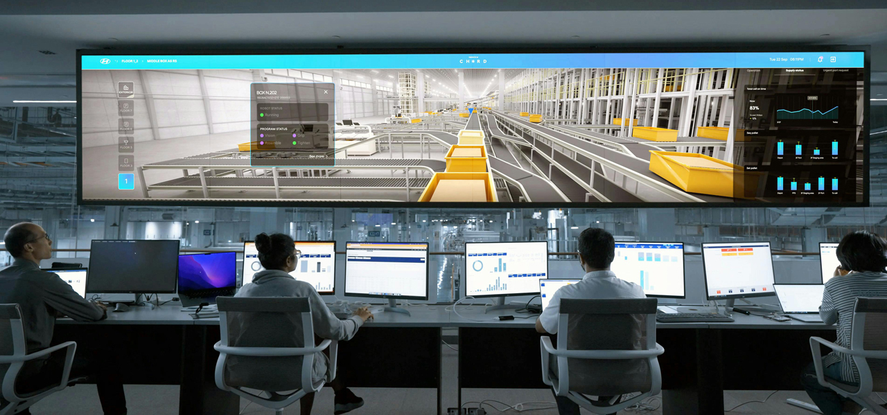 Several people look at a large screen and laptops