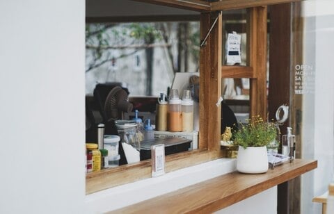 Open cafe window with potted plant, condiments, and kitchen supplies on a wooden counter.