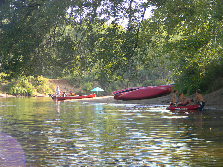 Canoë orange sur un lac calme entouré de montagnes et de forêt, ciel bleu et nuages.