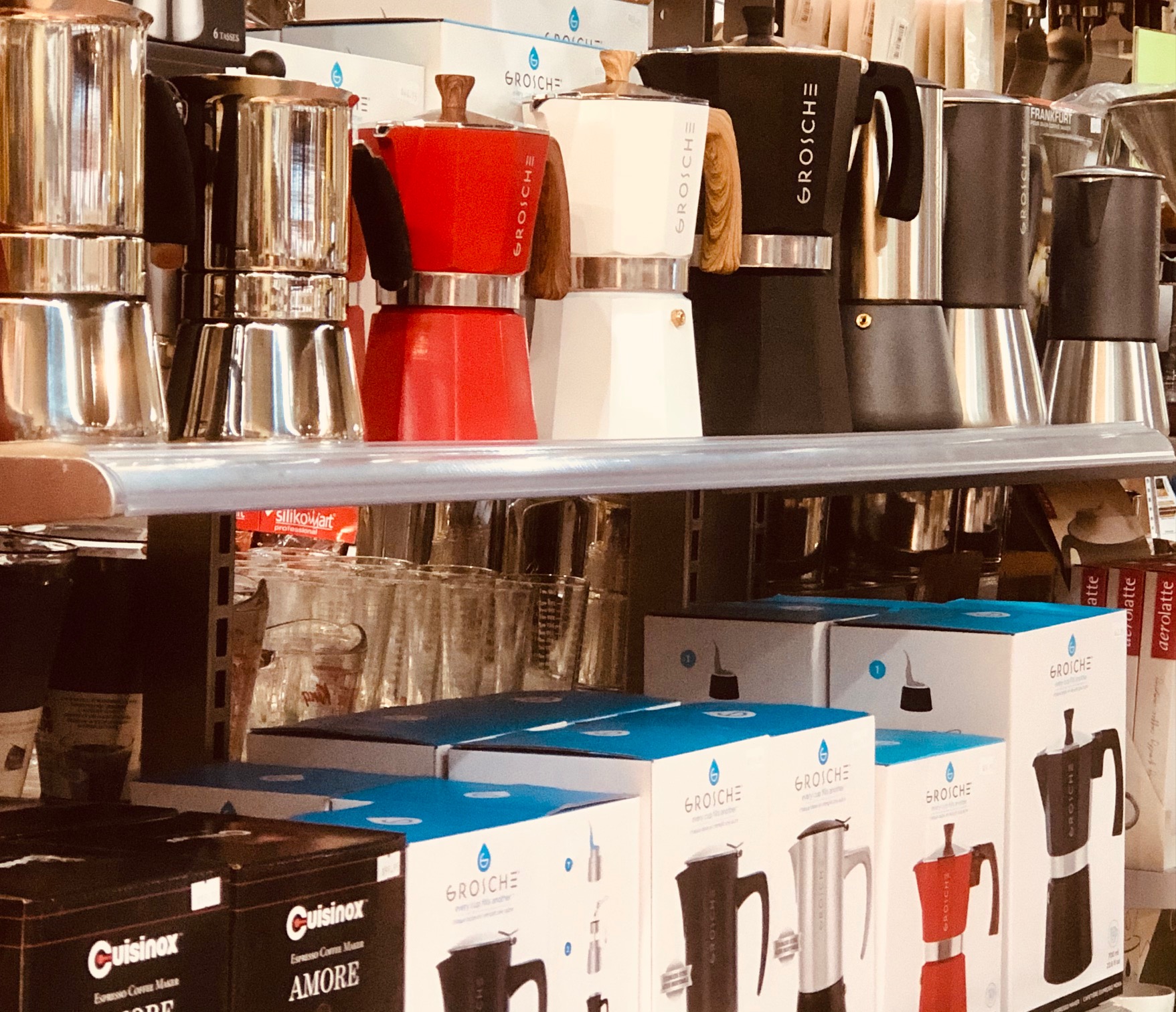 Shelf displaying various colorful moka pots and boxed coffee makers in a kitchenware store.