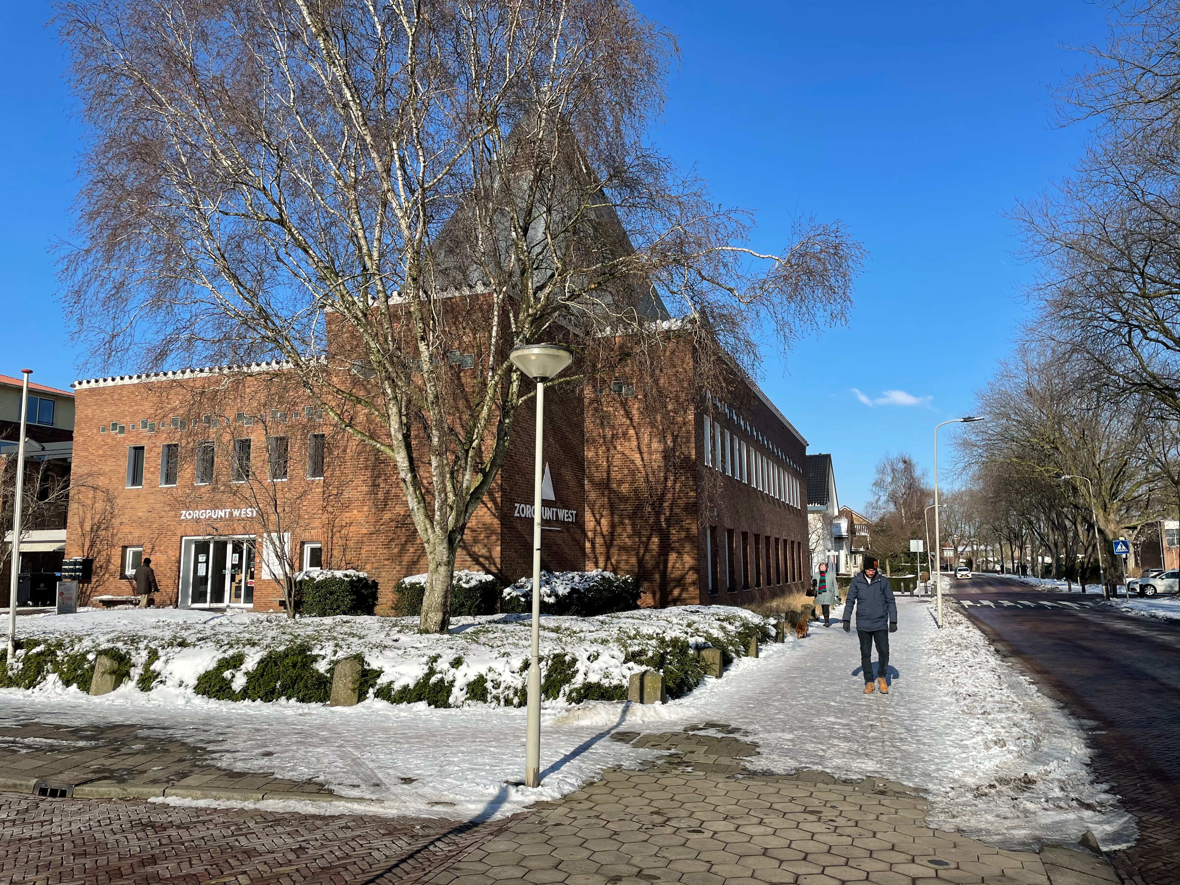 Zorgpunt West brick building on a snowy street with leafless trees under a clear blue sky