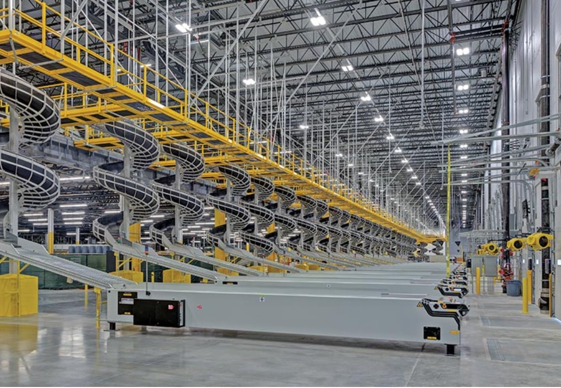 Interior view of a modern warehouse with multiple conveyor systems and overhead spiral chutes in an industrial setting.