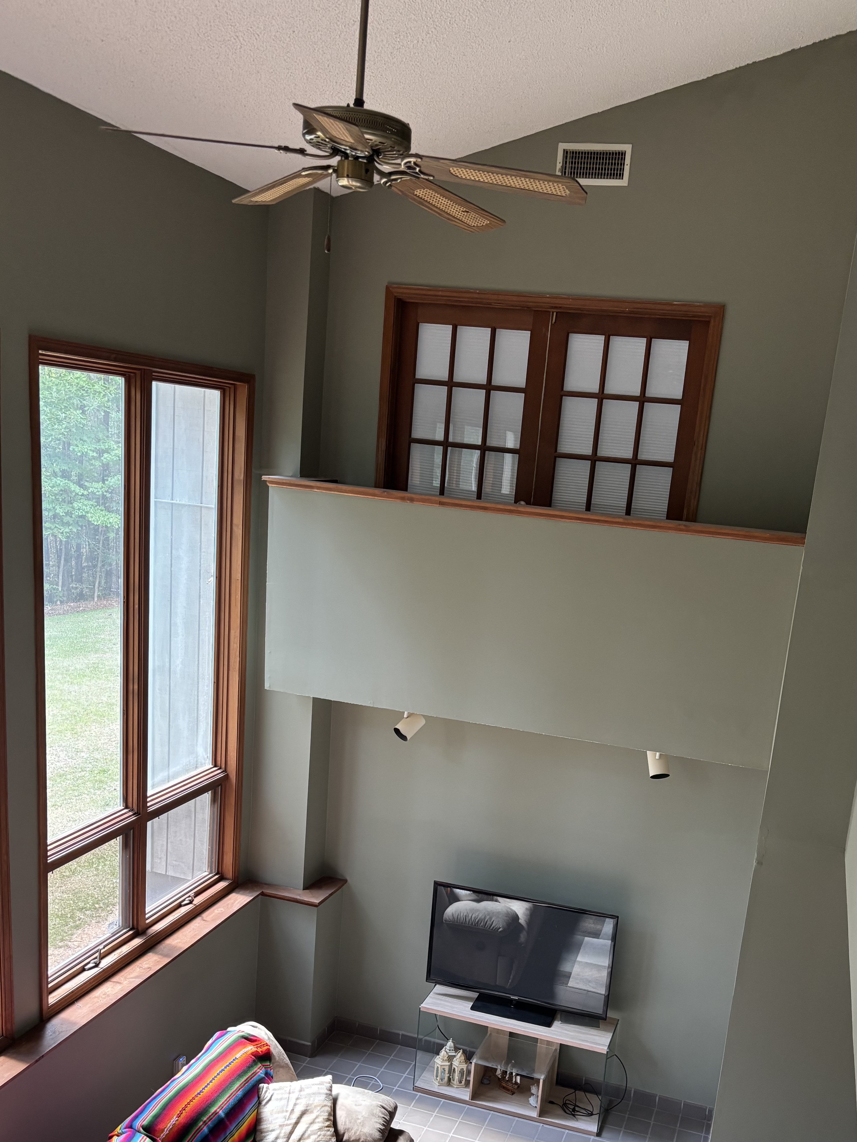 High ceiling living room with wooden ceiling fan, large windows, loft railing, and TV stand High ceiling living room with wooden ceiling fan, large windows, loft railing, and TV stand