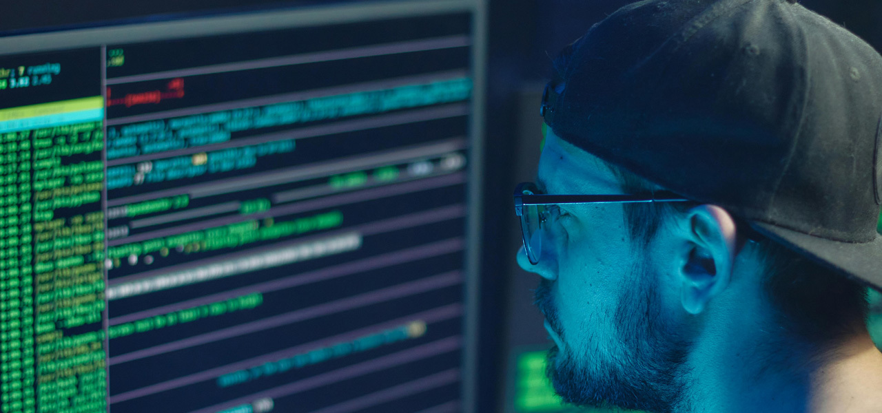 A man with a hat and glasses looking at a computer screen