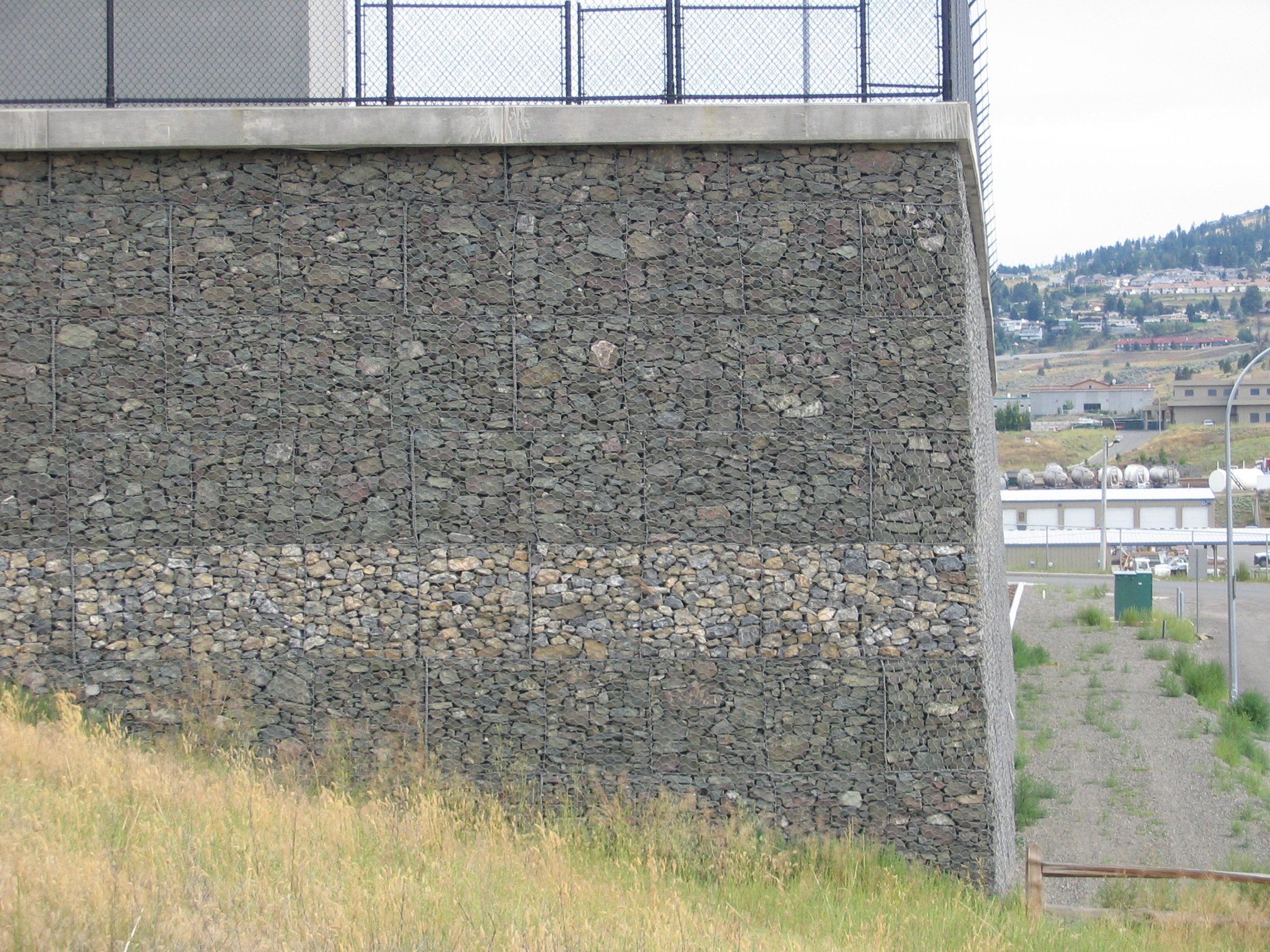 Modern building exterior with stone walls and metal staircase reflected in calm water.
